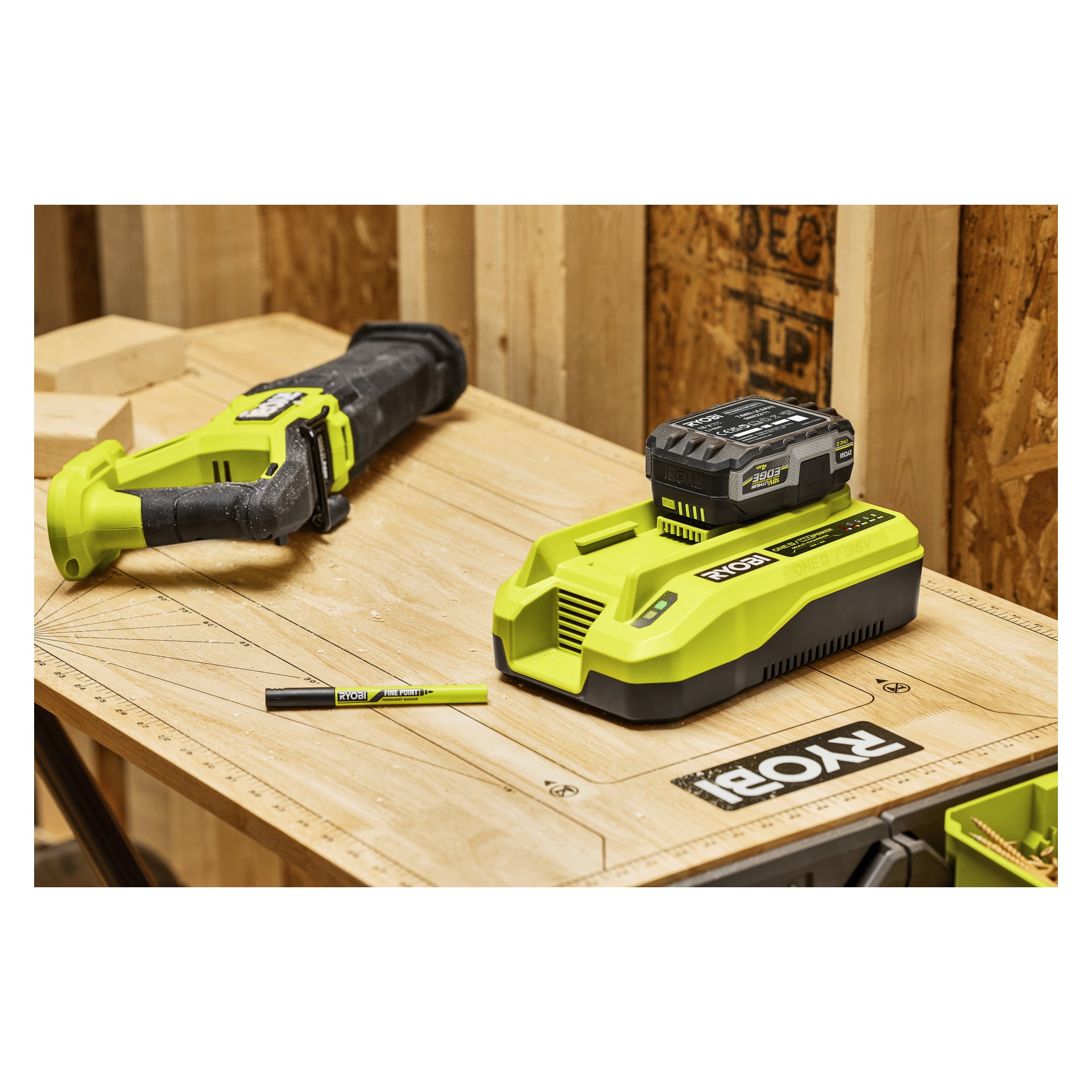 En Ryobi batteriladdare med batteri står på en träbänk bredvid en tigersåg och penna, med byggmaterial bakom.