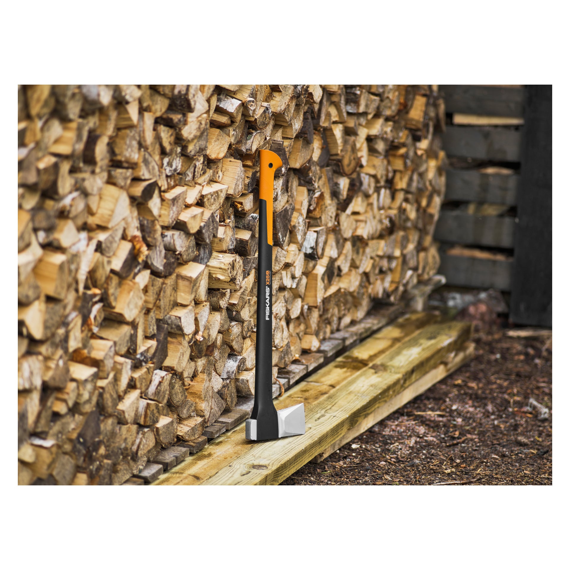 Ein spaltender Keil mit orange-schwarzem Griff ruht auf einem ordentlichen Stapel Feuerholz auf einer hölzernen Plattform im Freien.