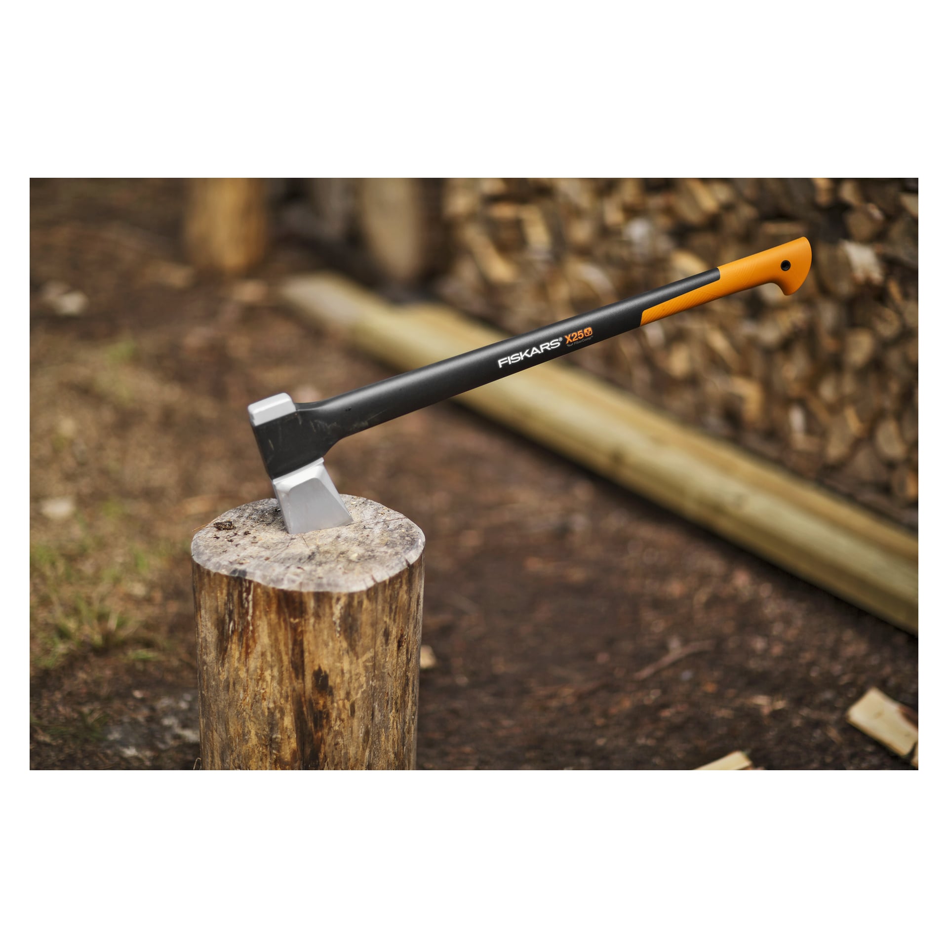 Ein Fiskars X25 Spaltaxt steckt aus einem Baumstumpf, mit gestapeltem Feuerholz und Baumstämmen, die draußen auf dem Boden verstreut liegen.