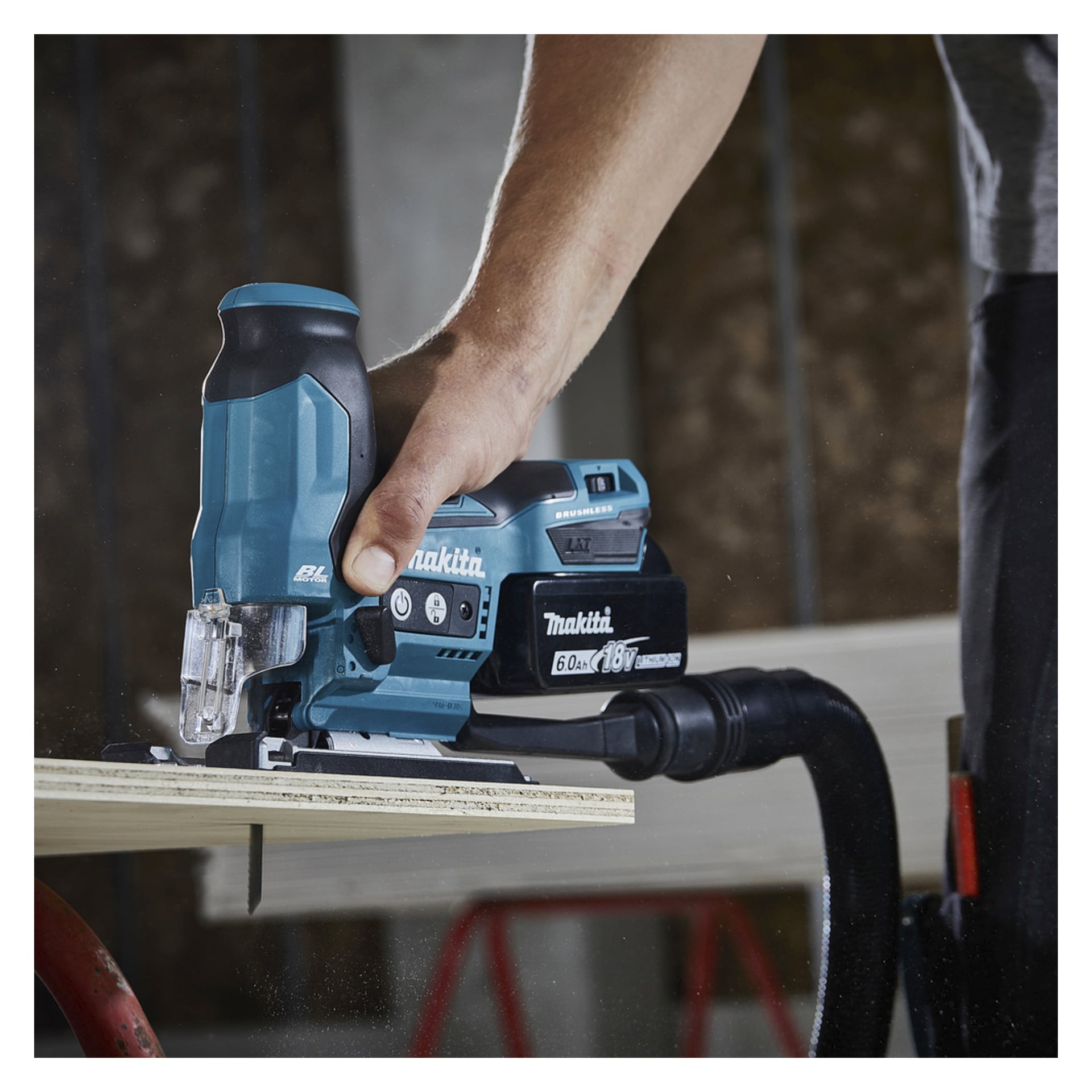 Någon använder en Makita sladdlös sticksåg med en dammavsugningsslang och kapar trä i bygg- eller snickerimiljö.