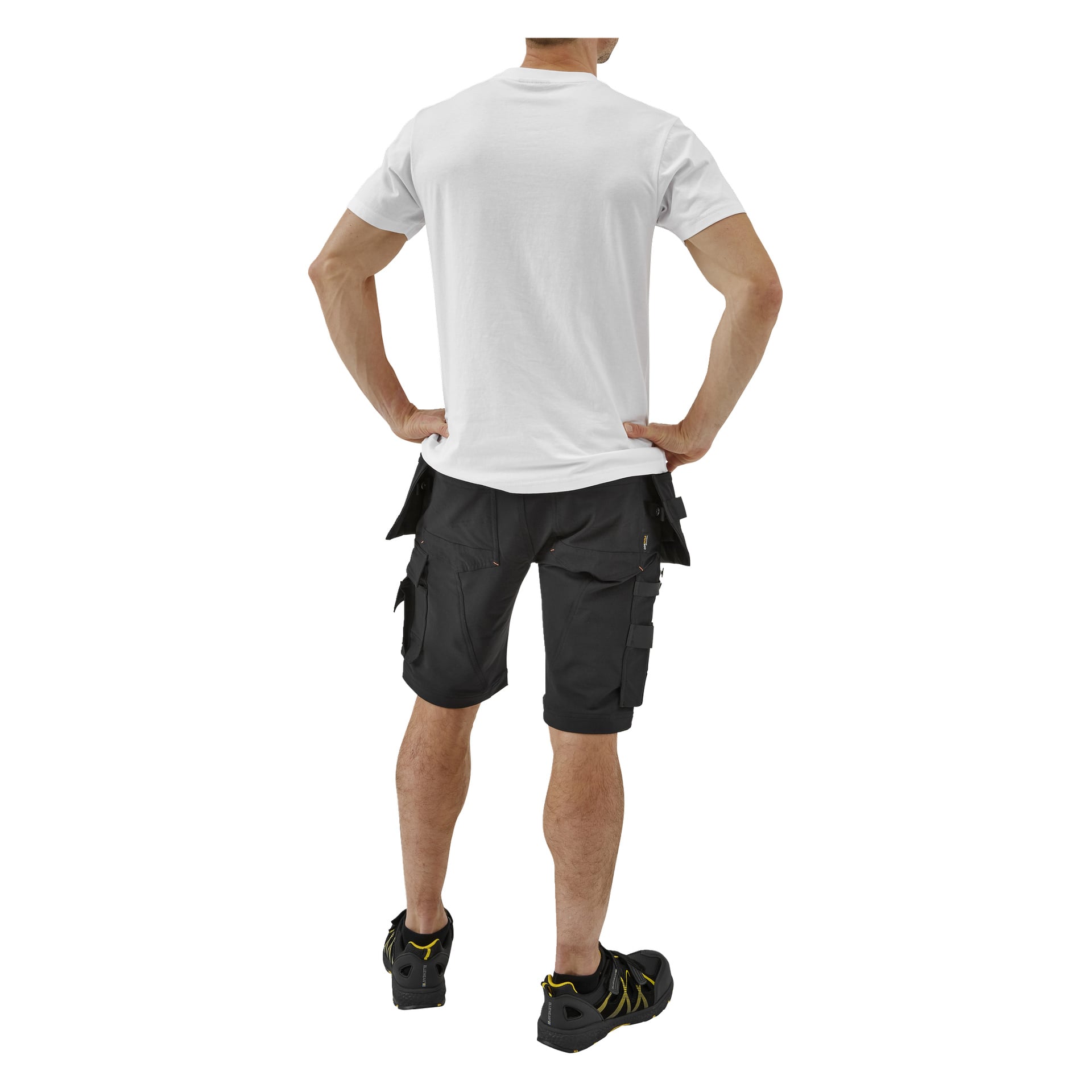 Sedd bakifrån står en person med händerna på höfterna i en vit T-shirt, svarta cargoshorts med fickor och svarta skor.