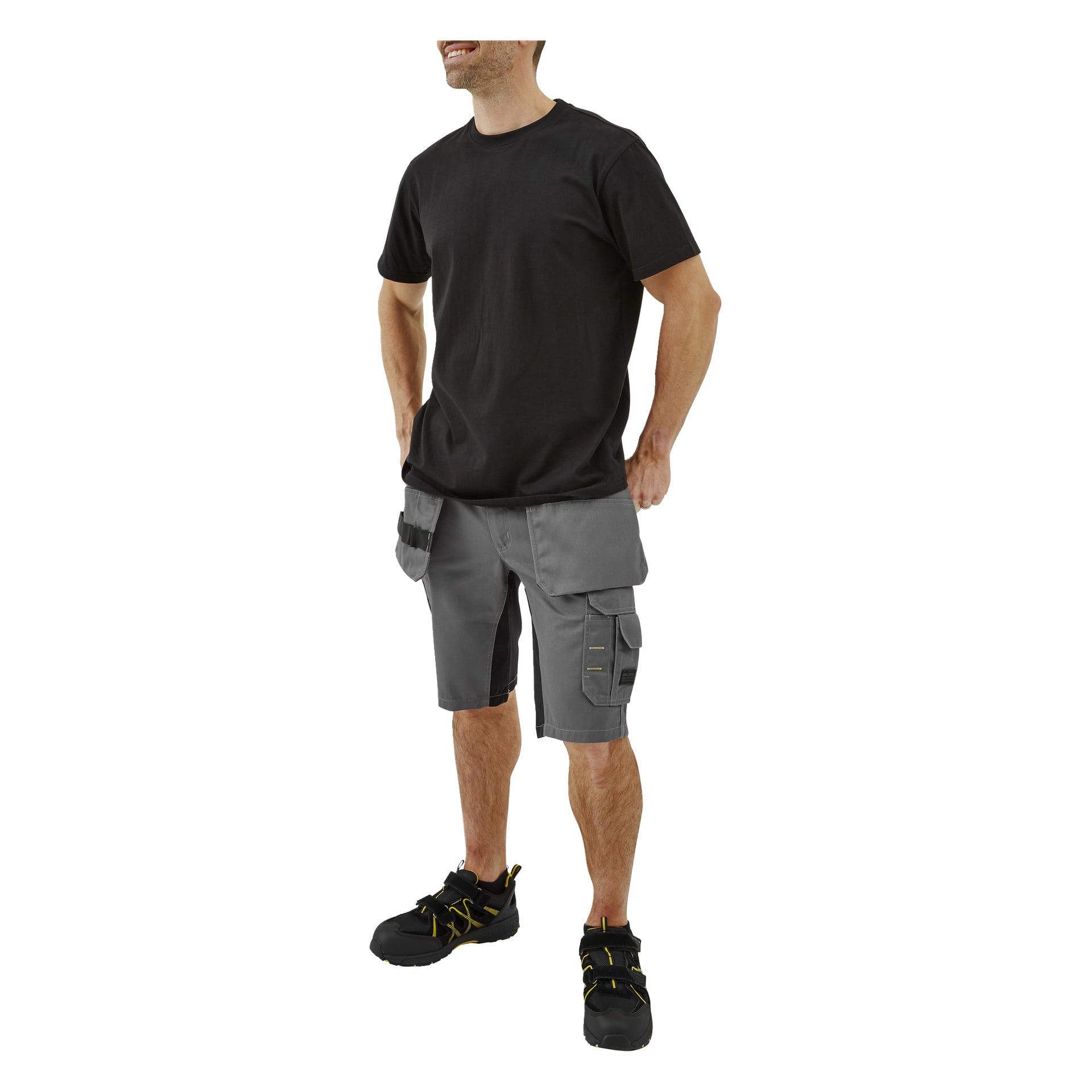 En leende man bär en enkel svart t-shirt, grå cargoshorts med fickor och öglor, samt svarta arbetsskor med gula detaljer.