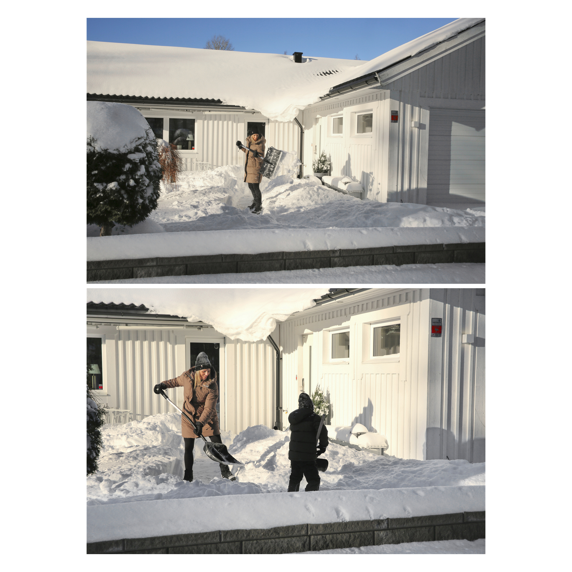 Två personer i vinterkläder skyfflar djup snö från en uppfart nära ett vitt hus en solig dag, snö täcker mark och tak.