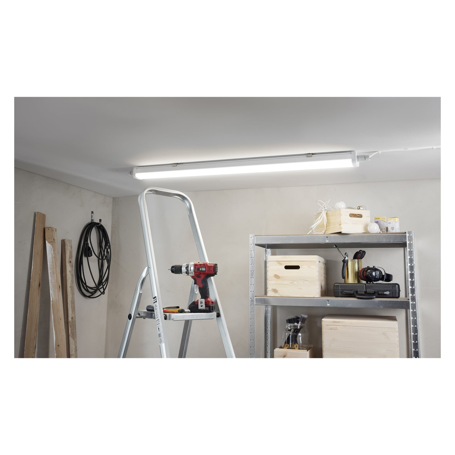 Eine Trittleiter und ein Akkubohrer befinden sich unter einer hellen Deckenlampe; In der Nähe lagern Kisten, Werkzeuge, Zwiebeln und Dielen.