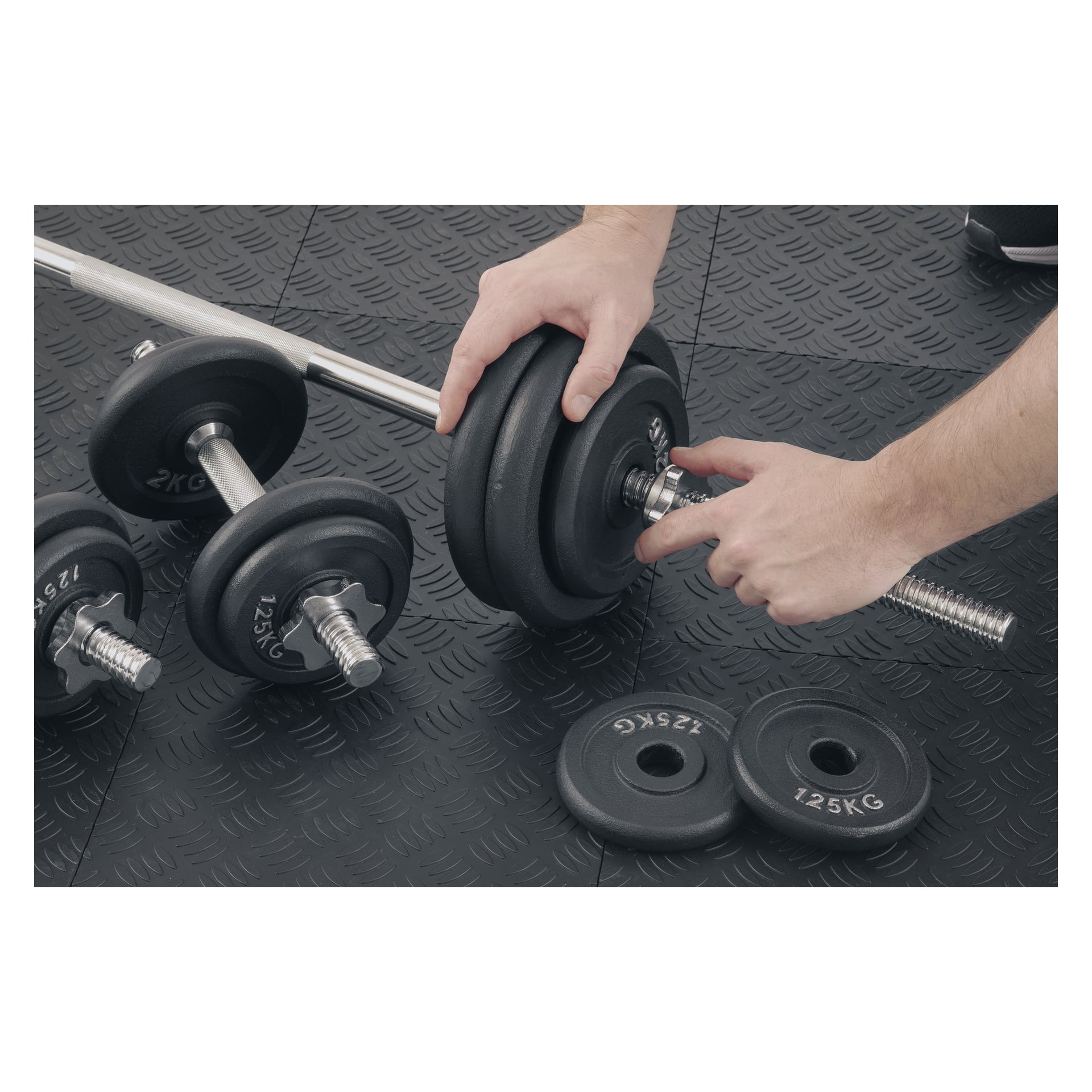 Händerna placerar en 1,25 kg platta på en skivstång; Ytterligare skivstänger och plattor vilar på ett svart gymgolv med struktur i närheten.