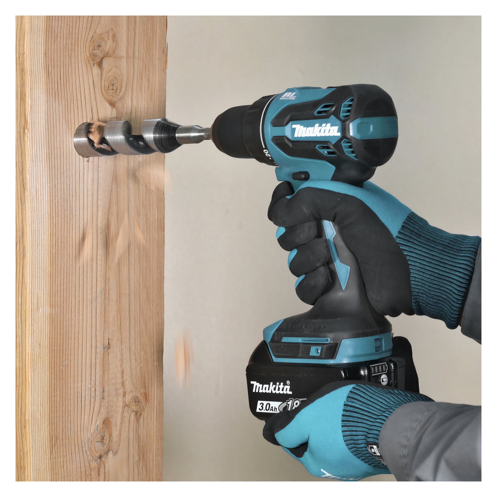 En person i blå handskar borrar ett hål i en vertikal träbalk med hjälp av en sladdlös Makita-borrmaskin med en stor borr.