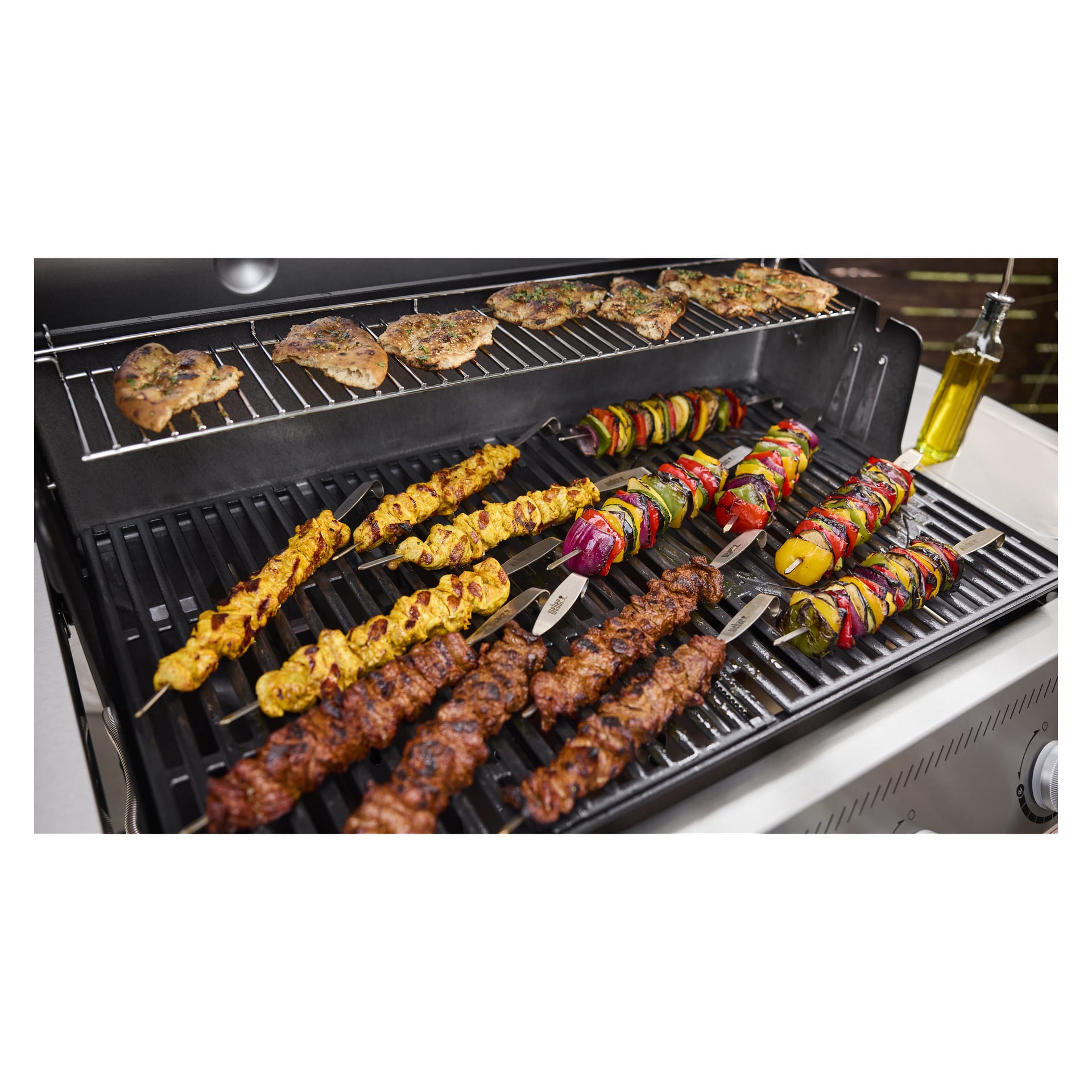 Kilka szaszłyków z mięsem, warzywami i grillowanym kurczakiem piecze się na grillu, a butelka oliwy z oliwek stoi w pobliżu.