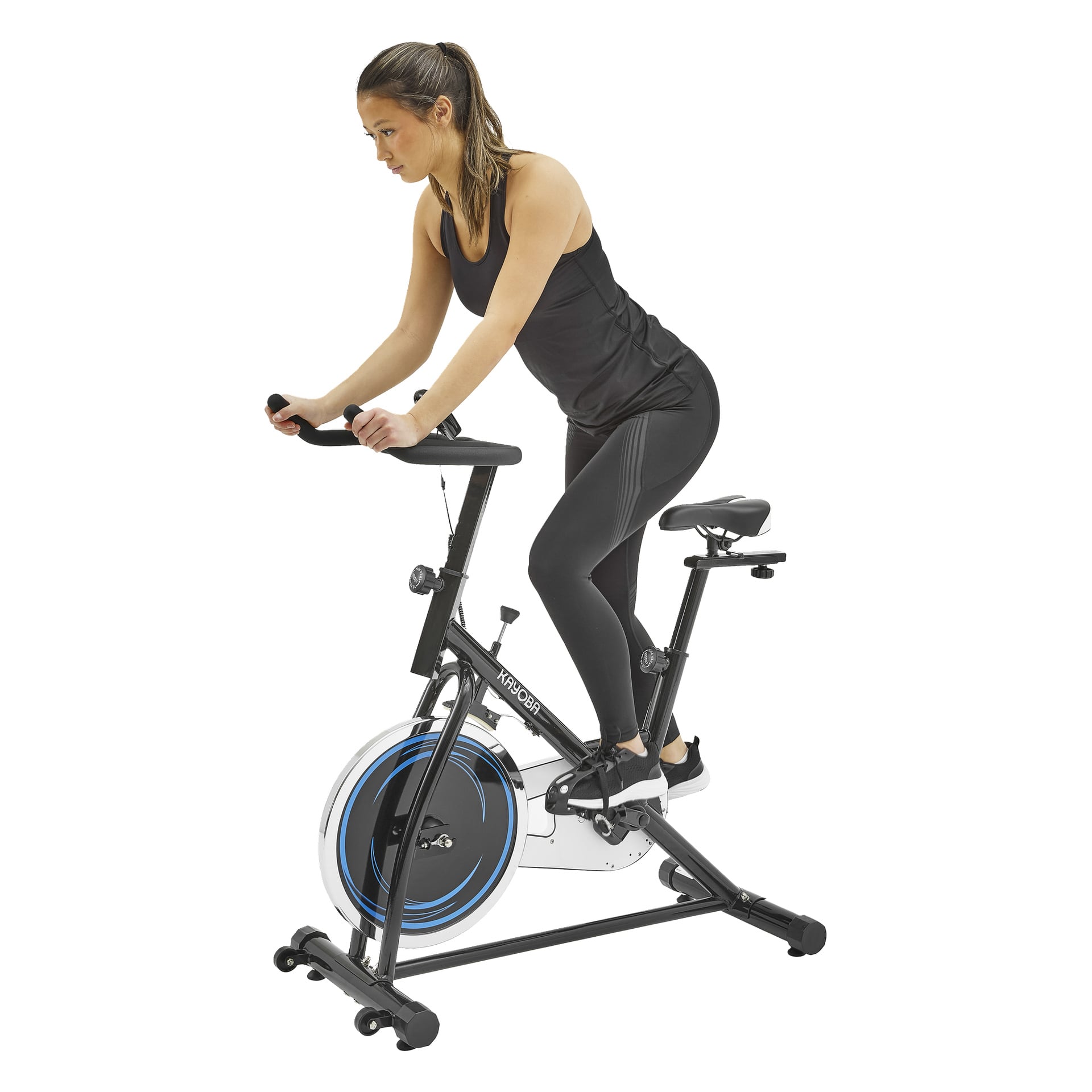 En person i svart träningsutrustning trampar på en motionscykel med blå detaljer och ett cirkulärt svänghjul, håller styret och håret är uppsatt bakåt.