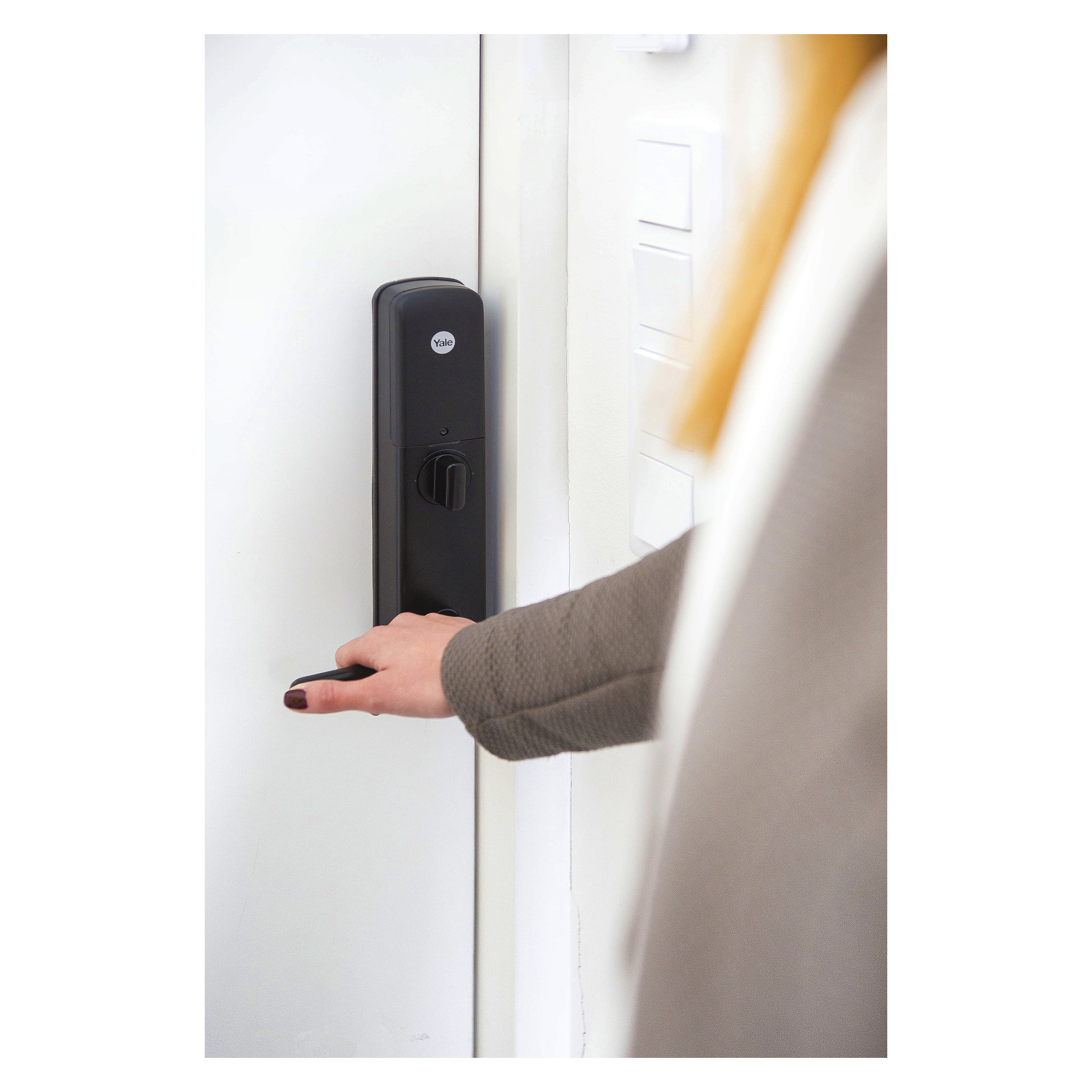 En person i en grå blazer holder håndtaket på en hvit dør med svart elektronisk lås.