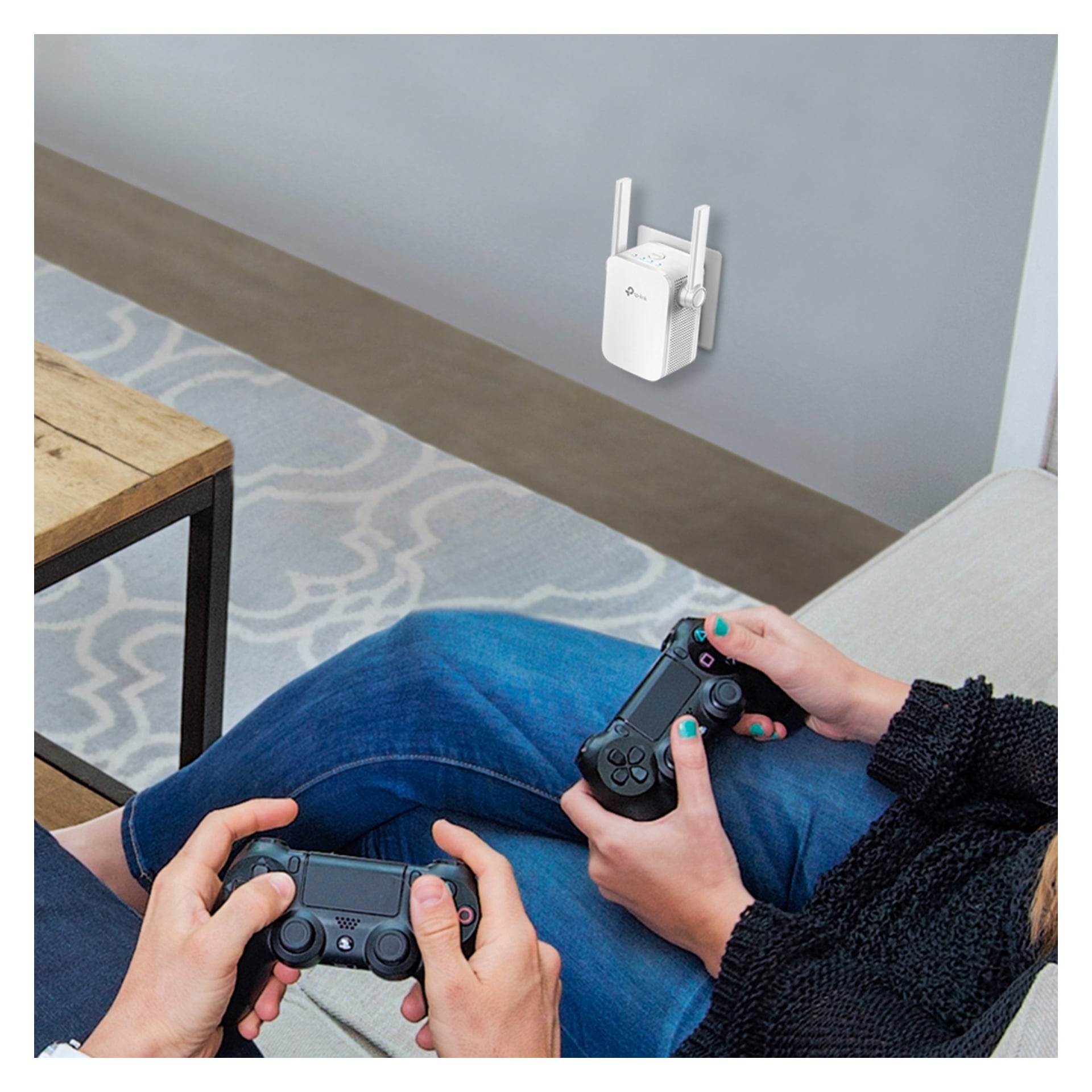 Två personer i en soffa spelar videospel med handkontroller; en Wi-Fi-förlängare finns i ett närliggande uttag, nära ett träbord och en matta.