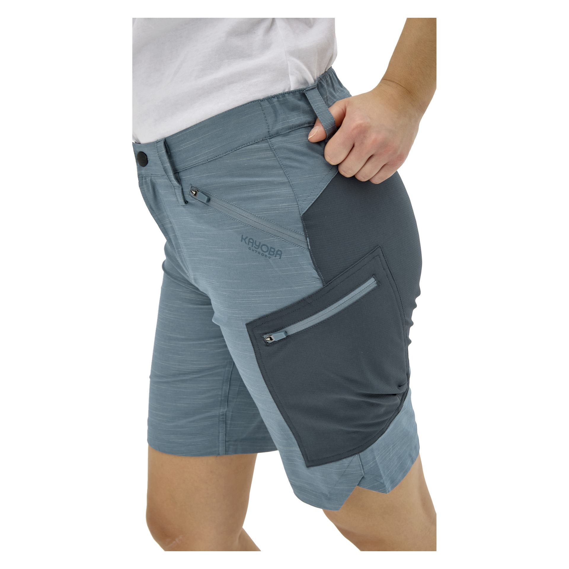 En person i ljusblågrå shorts med mörkgrå paneler och flera fickor, plus en vit skjorta. KAYOBA-logotypen syns på shortsen.