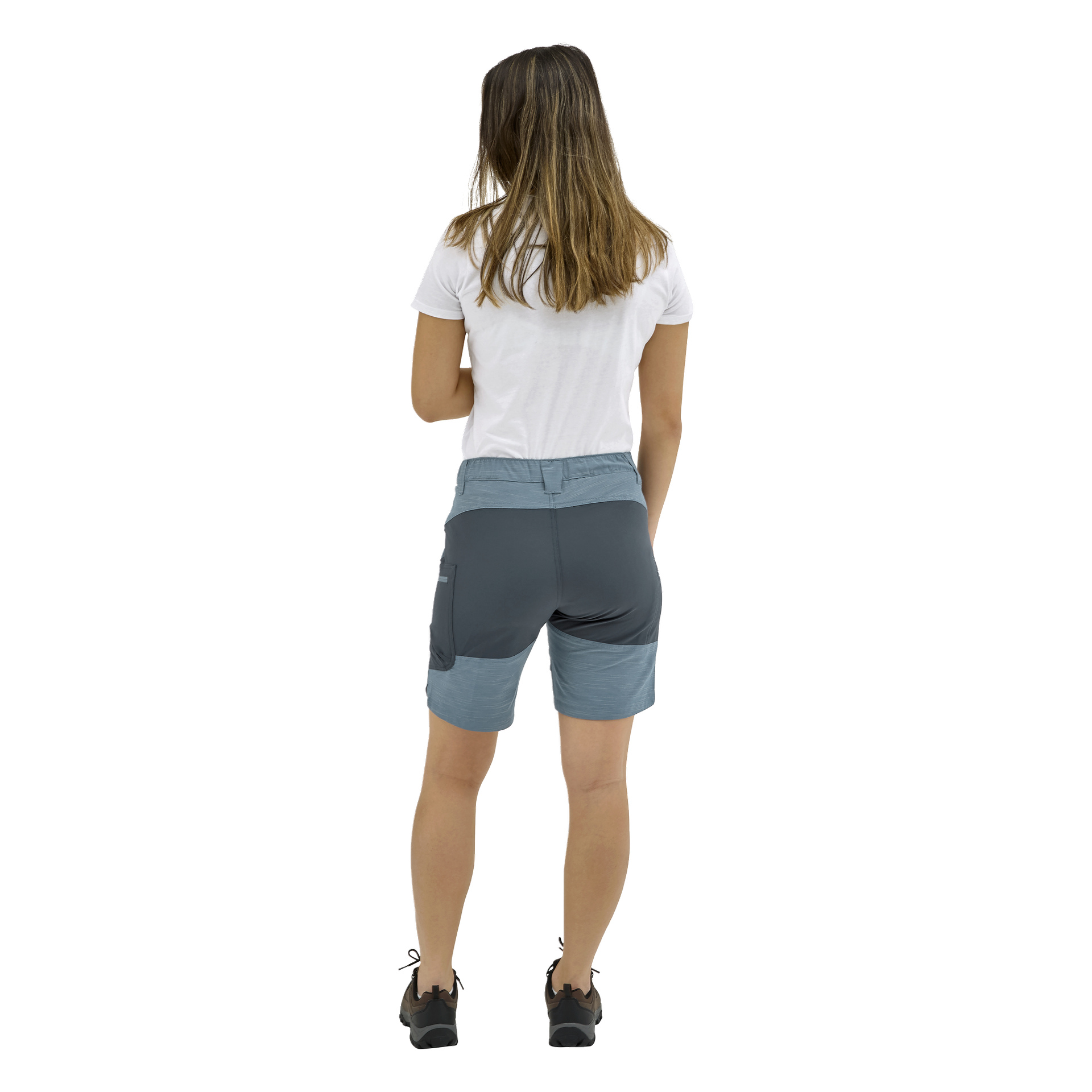 En kvinna med rakt axellångt hår står vänd bort, klädd i en vit t-shirt, blågrå shorts och svarta sneakers.