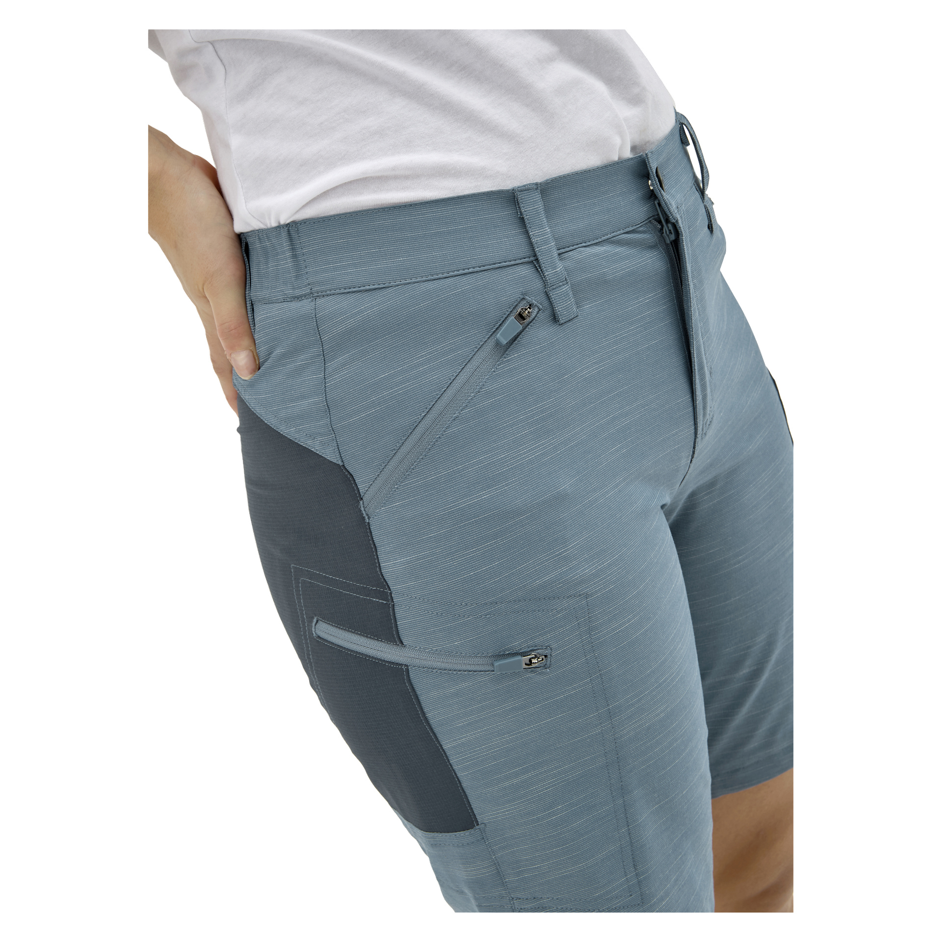 Någon i ljusblå skräddarsydda shorts med dragkedjefickor och en vit skjorta står med ena handen på höften.