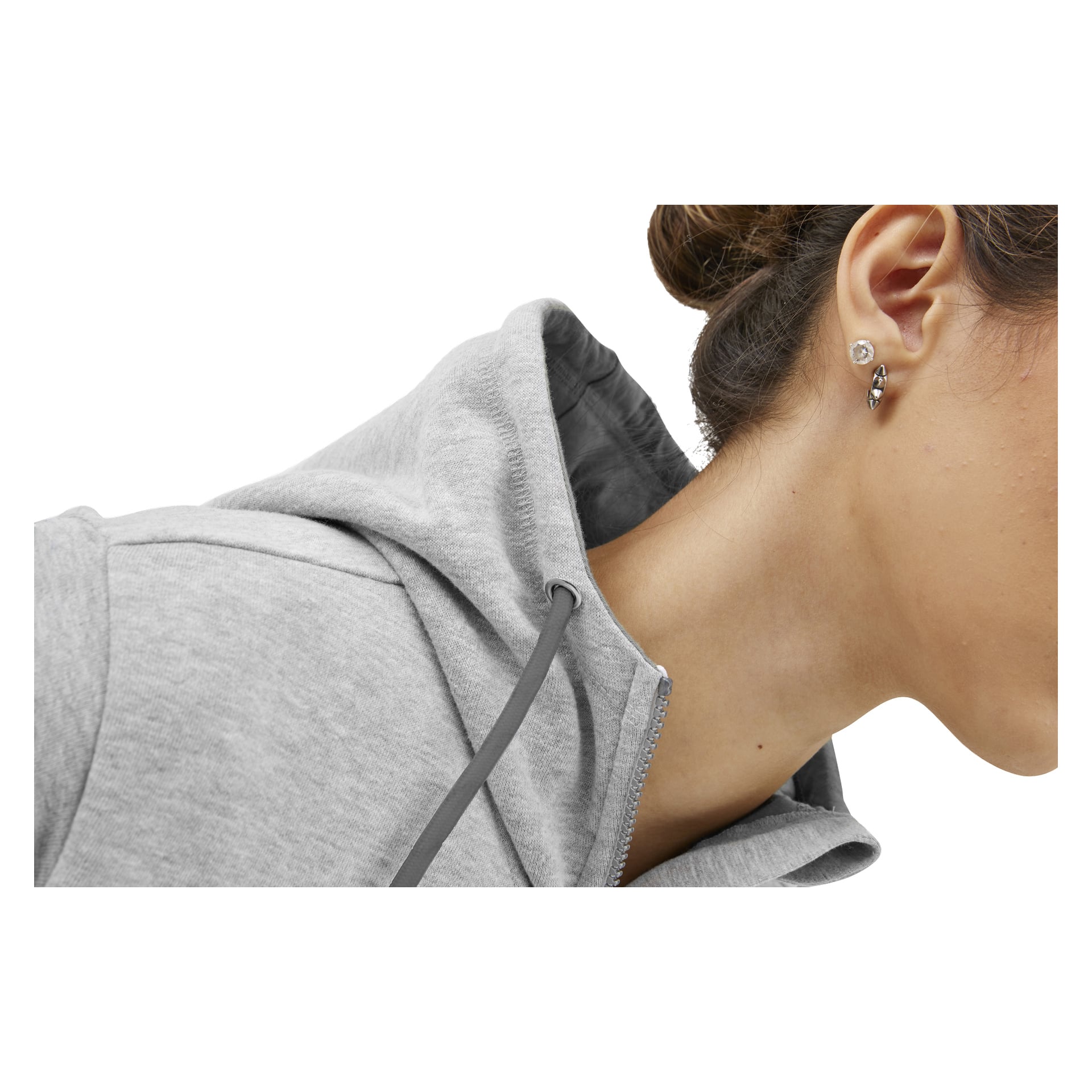 Närbild på en person i en ljusgrå hoodie, som visar sidan av ansiktet, örat med örhänge och uppsatt hår.