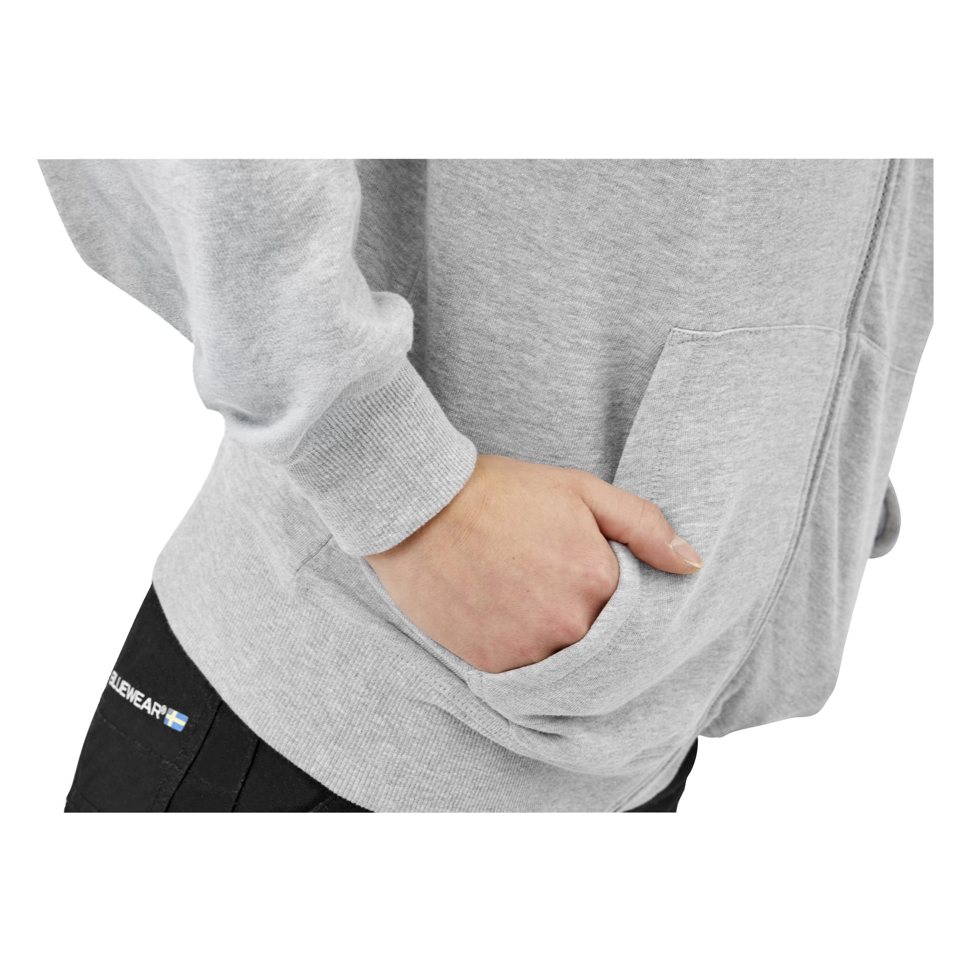 Någon klädd i en ljusgrå zip-up hoodie och svarta byxor vilar höger hand i fickan; Ryckiga muddar och en liten byxetikett.
