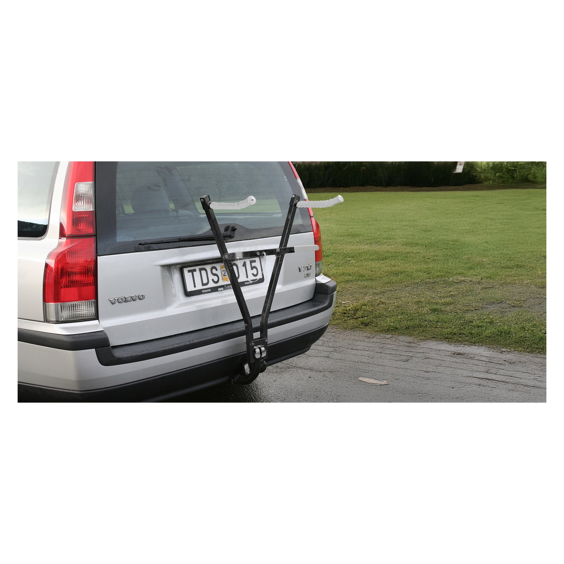 En silverfärgad Volvo kombi med registreringsskylt TDS 15 och ett svart bakre cykelställ står parkerad på våt asfalt bredvid en gräsmatta.