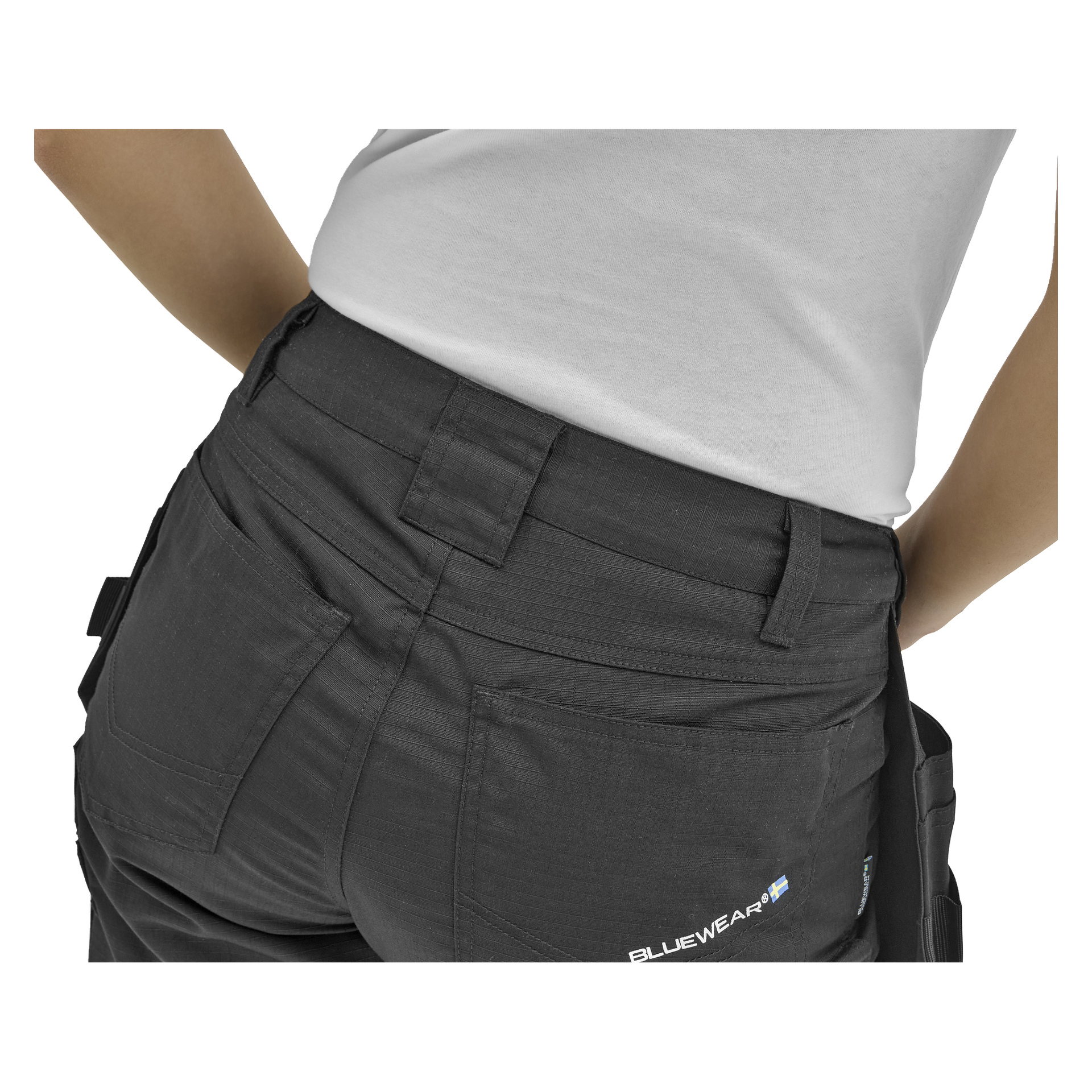Die Person trägt ein weißes Hemd und dunkelgraue BLUEWEAR-Arbeitshosen mit einer Hand auf der Hüfte, sichtbar von der Taille bis zum oberen Bein.