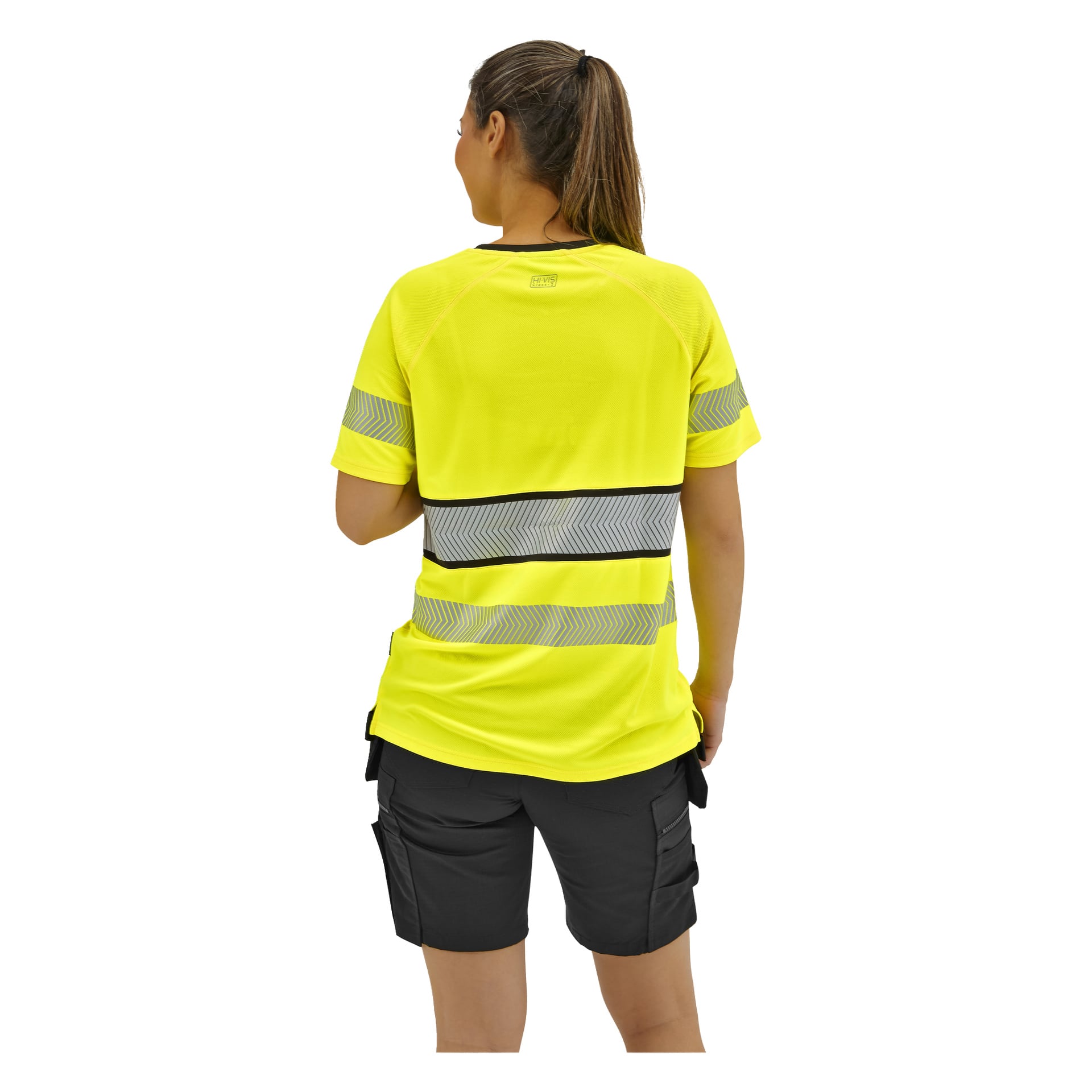 Personen med hästsvans i en gul högsynlig tröja och svarta cargoshorts står vänd bort från kameran.