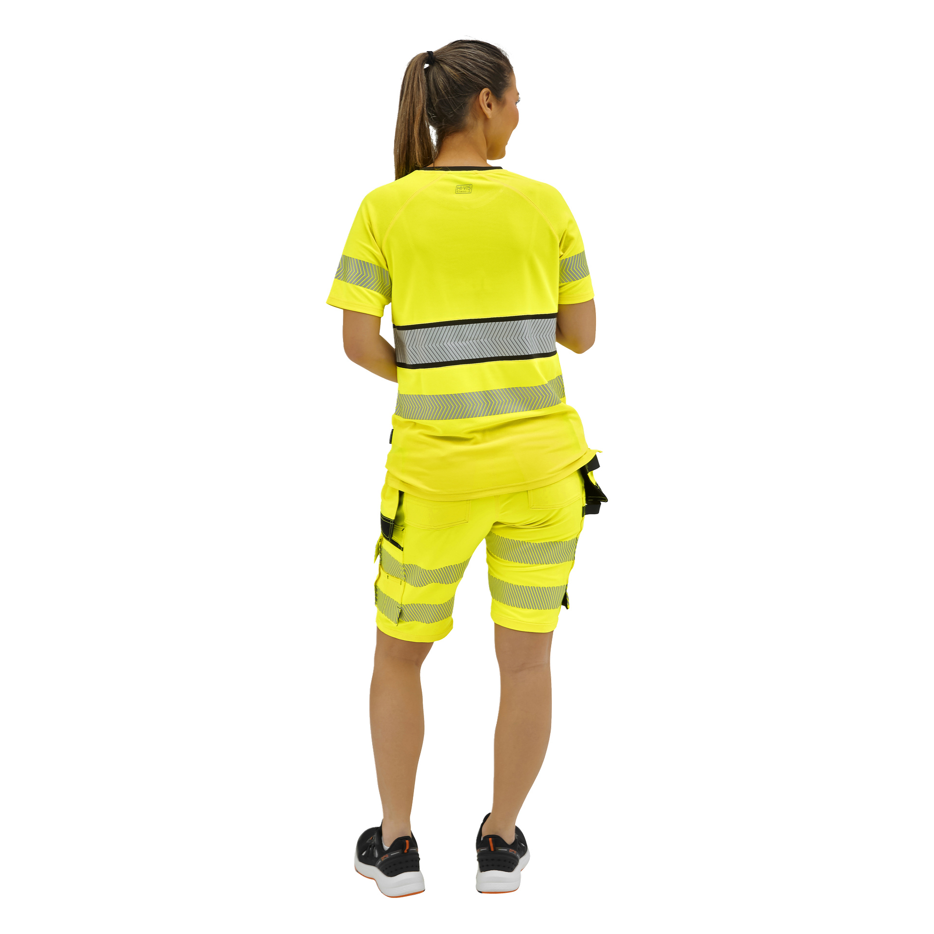 Eine von hinten gesehene Person mit Pferdeschwanz trägt ein neongelbes Sicherheitsoutfit mit reflektierenden Streifen, Cargoshorts und schwarze Turnschuhe.