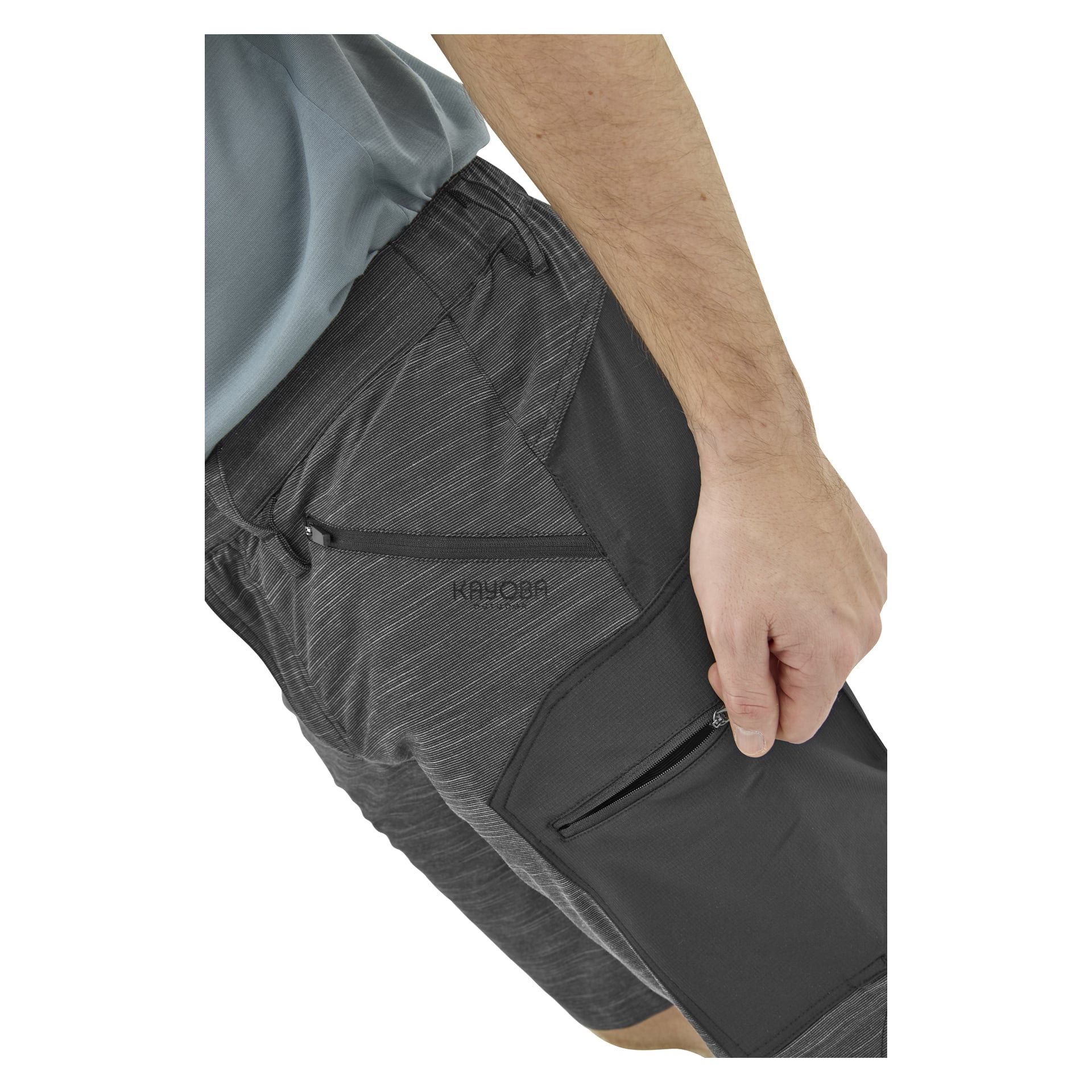 En person i mörkgrå, subtilt randiga shorts med fickor med dragkedja, synlig från midja till mitten av låret, höger hand vilande nära en ficka.