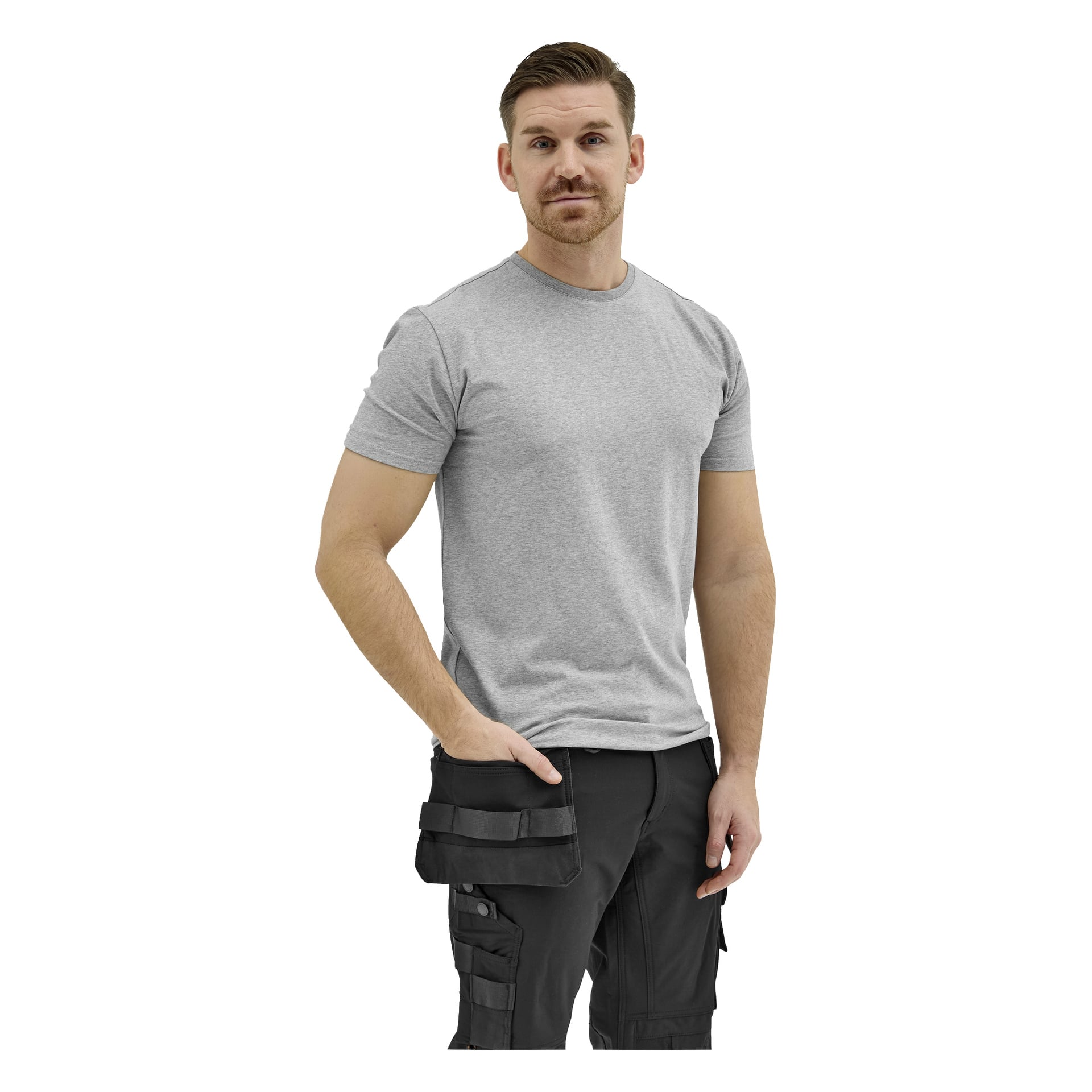 En skäggig man med kort hår står vänd framåt i en ljusgrå t-shirt och svarta cargobyxor, armarna avslappnade vid sidorna.