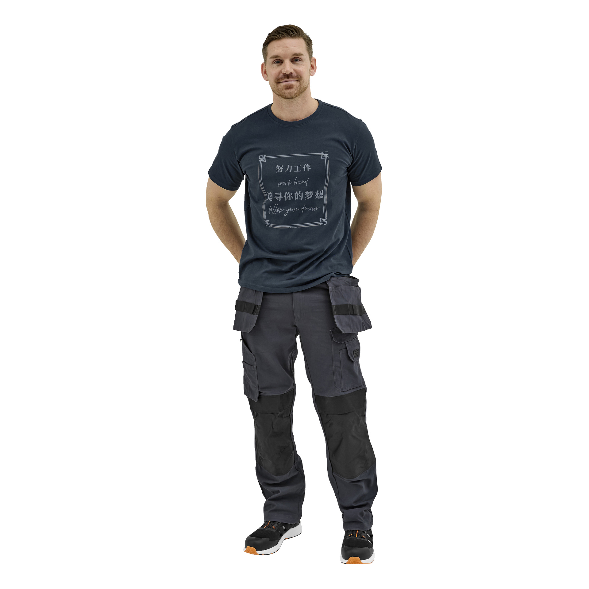 En mann med kort hår og skjegg står, med et svakt smil, iført en marineblå t-skjorte med sitat, mørke cargobukser og svart-oransje joggesko.