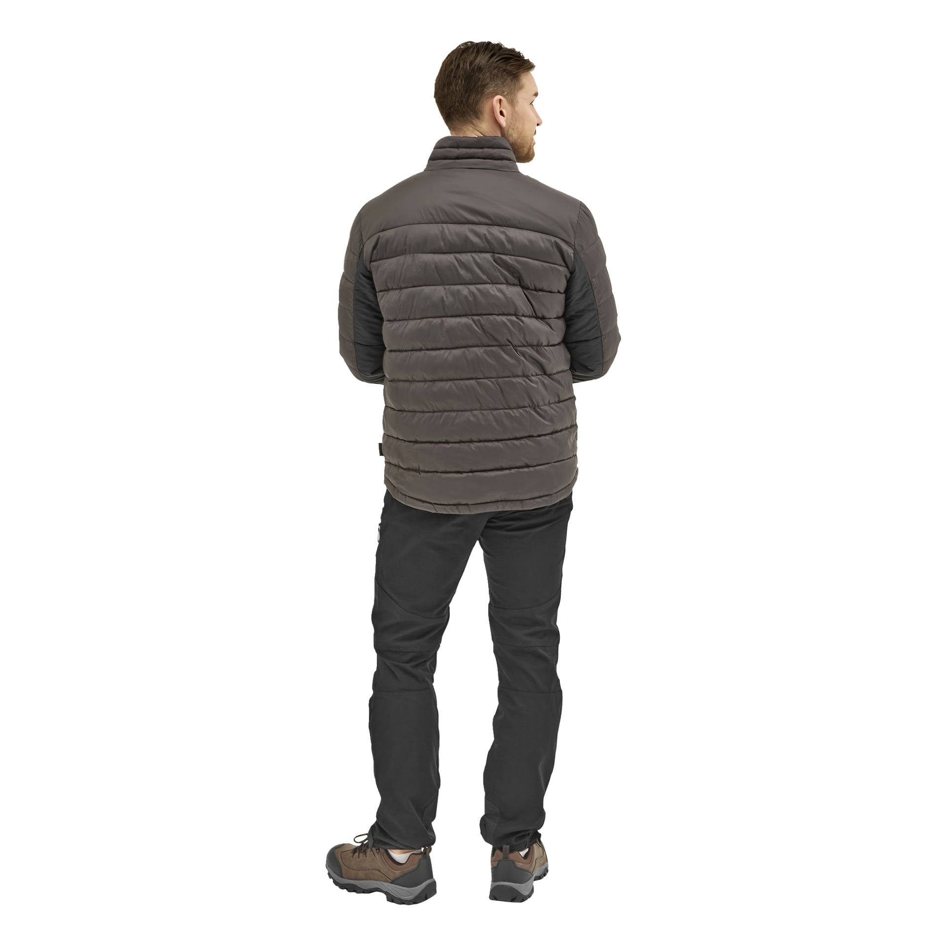 En man vänder blicken bort från kameran i en grå dunjacka, svarta byxor och bruna och svarta skor.