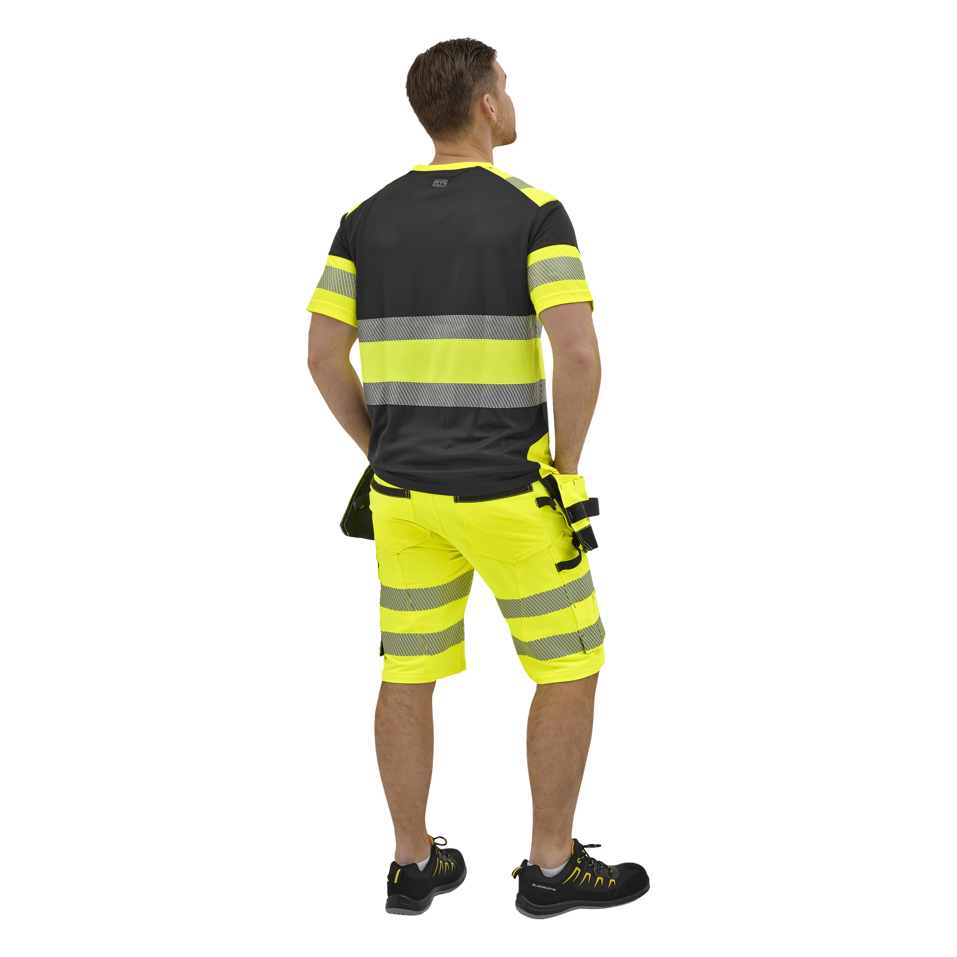 En man vänder sig bort, klädd i en svart och neongul kortärmad skjorta, neongula arbetsshorts med reflekterande ränder och svarta skor.