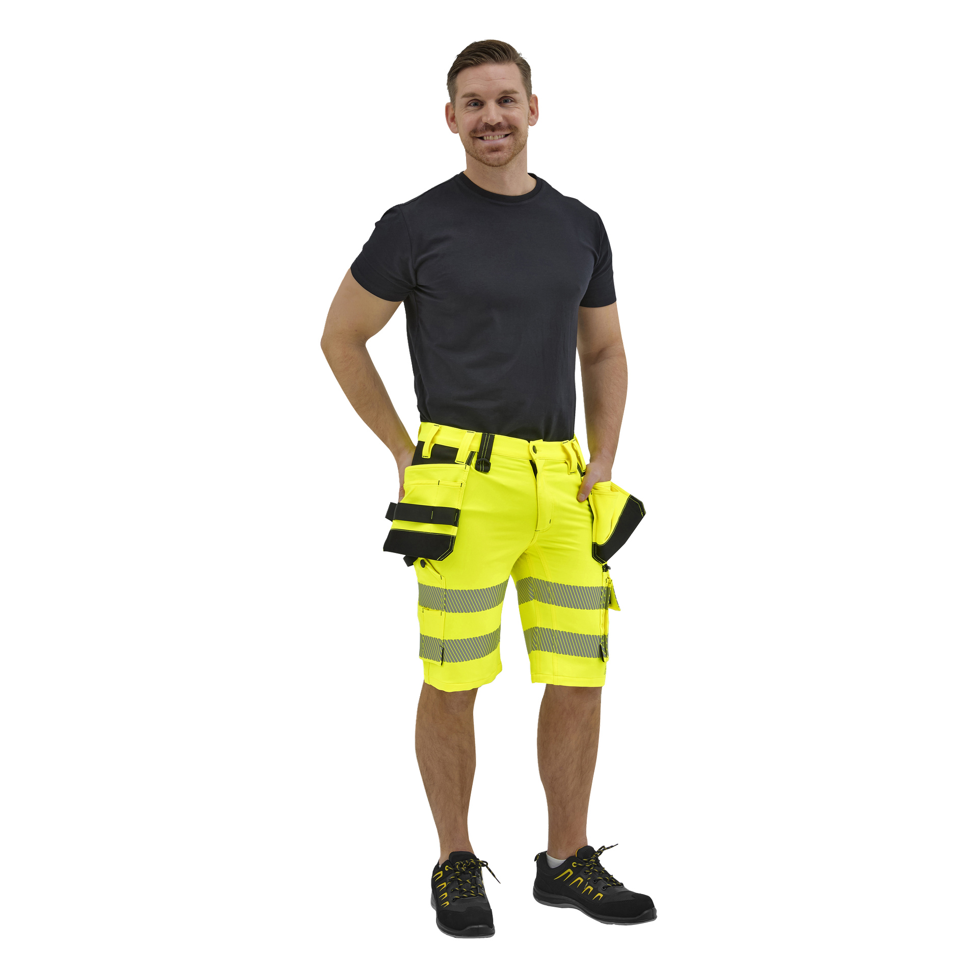 Leende man i svart t-shirt, neongula arbetsshorts med reflekterande ränder och fickor, och svarta skor med gula detaljer.