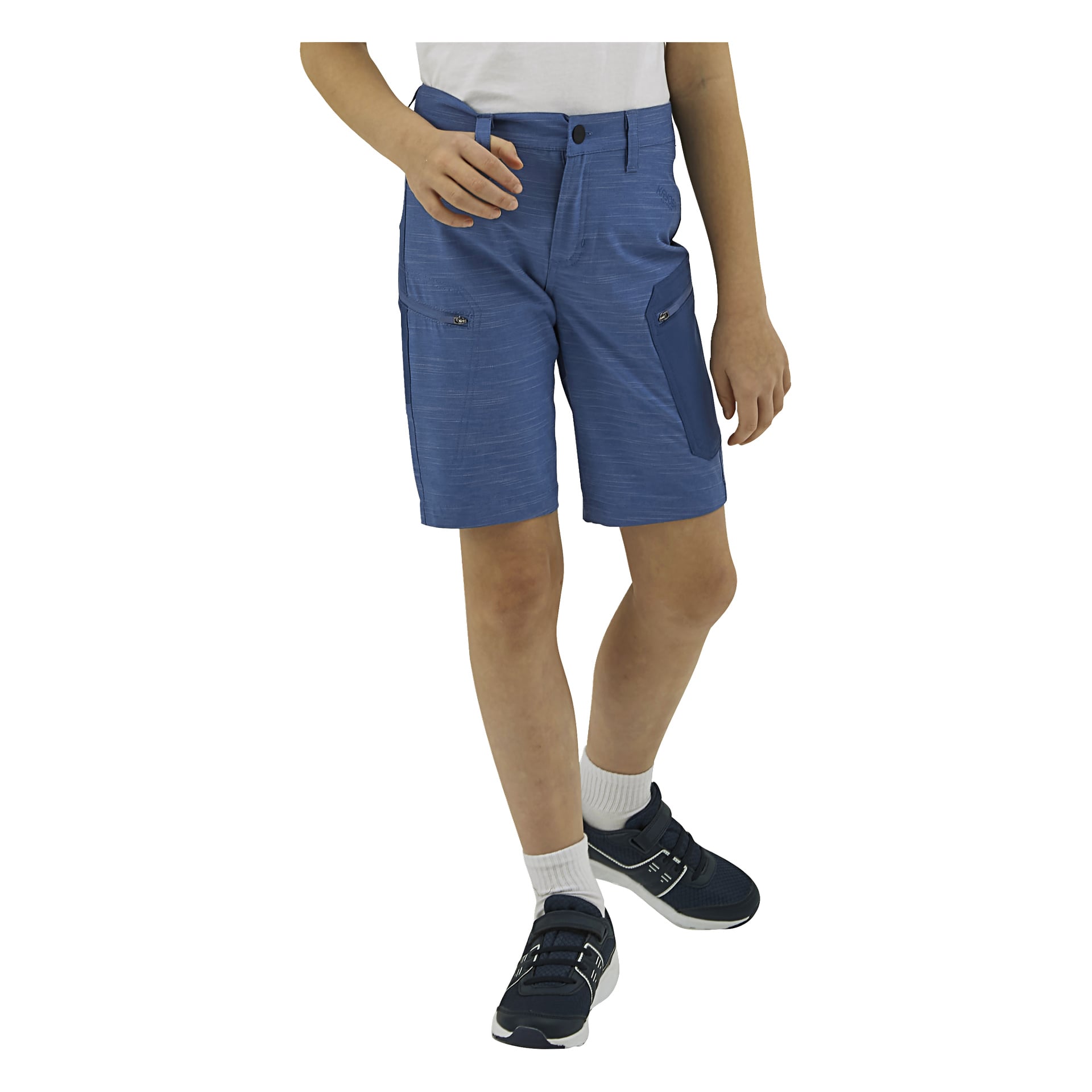 Ett barn i blå knälånga shorts med dragkedjefickor, en vit skjorta, vita strumpor och mörkblå sneakers.