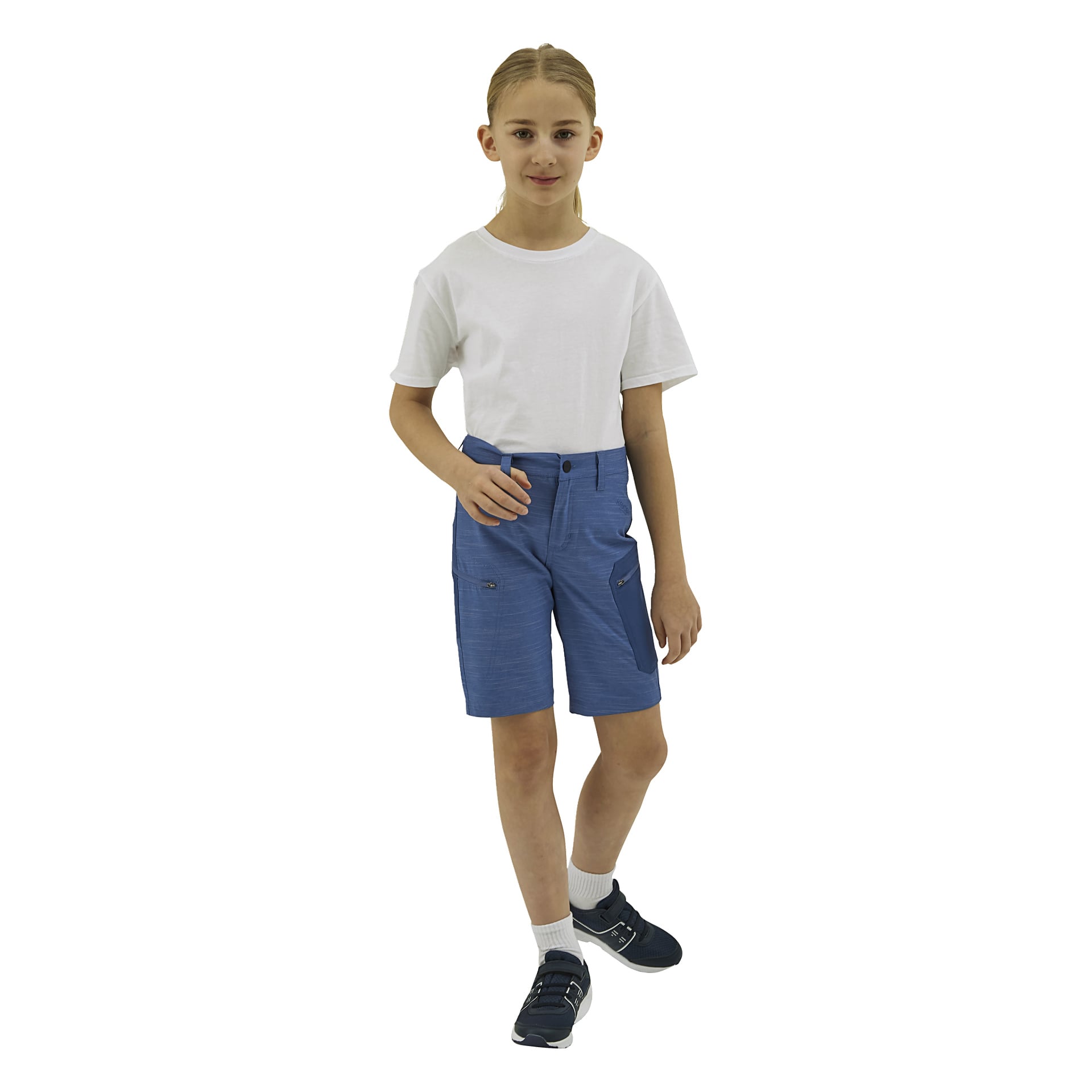Ett barn med långt, ljusbrunt hår bär en vit t-shirt, blå shorts med fickor, vita strumpor och marinblå sneakers, med blicken framåt.