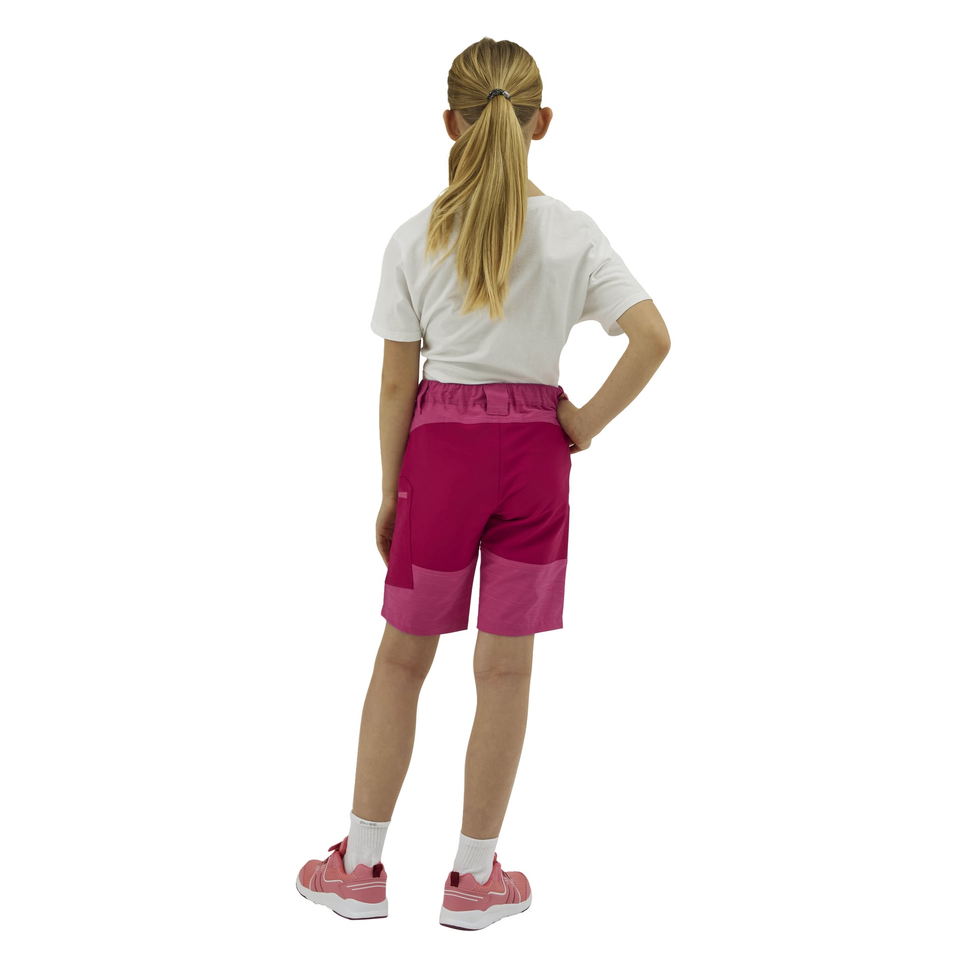 En flicka vänder sig bort, klädd i en vit t-shirt, rosa shorts, vita strumpor och rosa sneakers. Hennes blonda hår är i hästsvans.