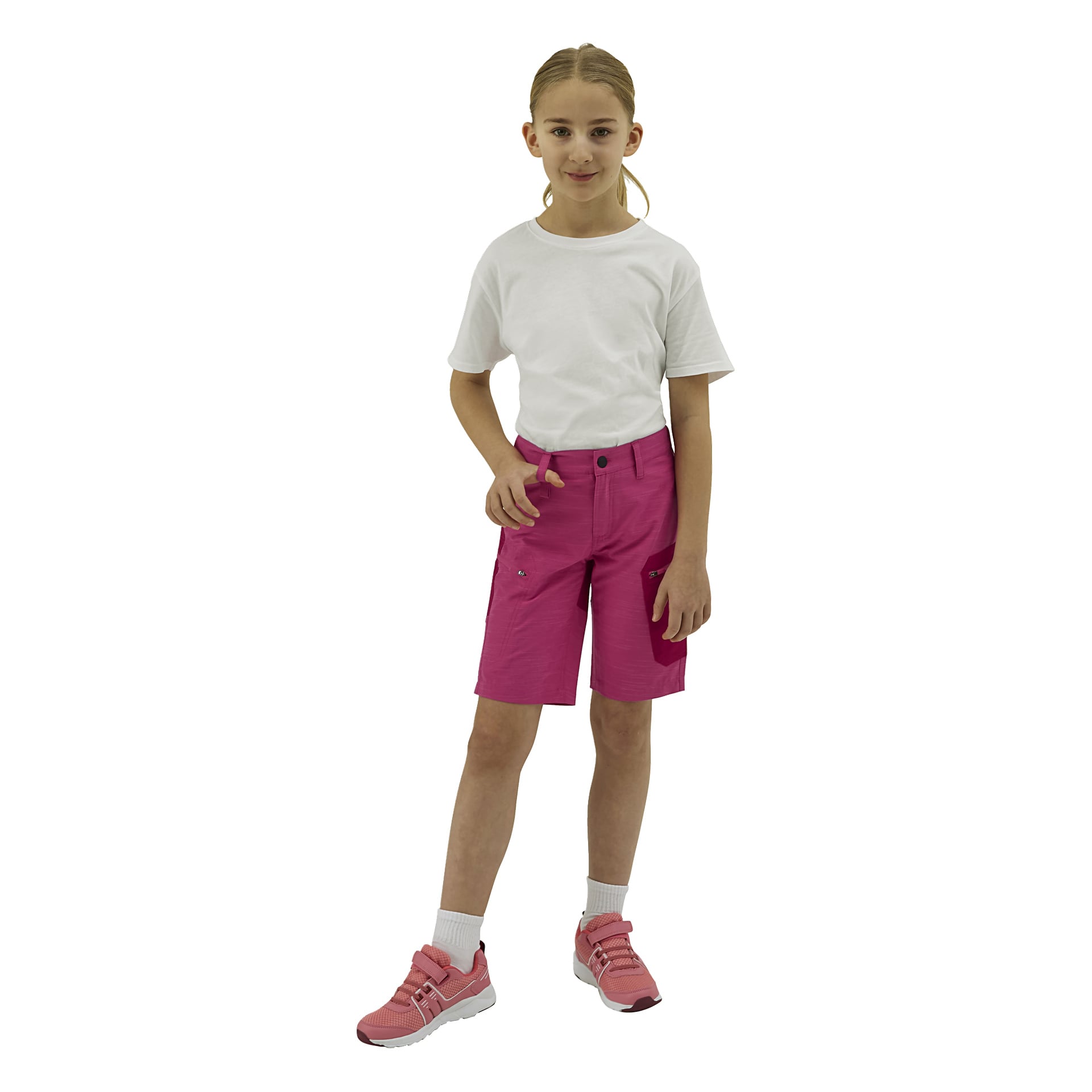 Ett barn med blont hår i hästsvans står iklädd en vit t-shirt, knallrosa shorts, vita strumpor och rosa sneakers.