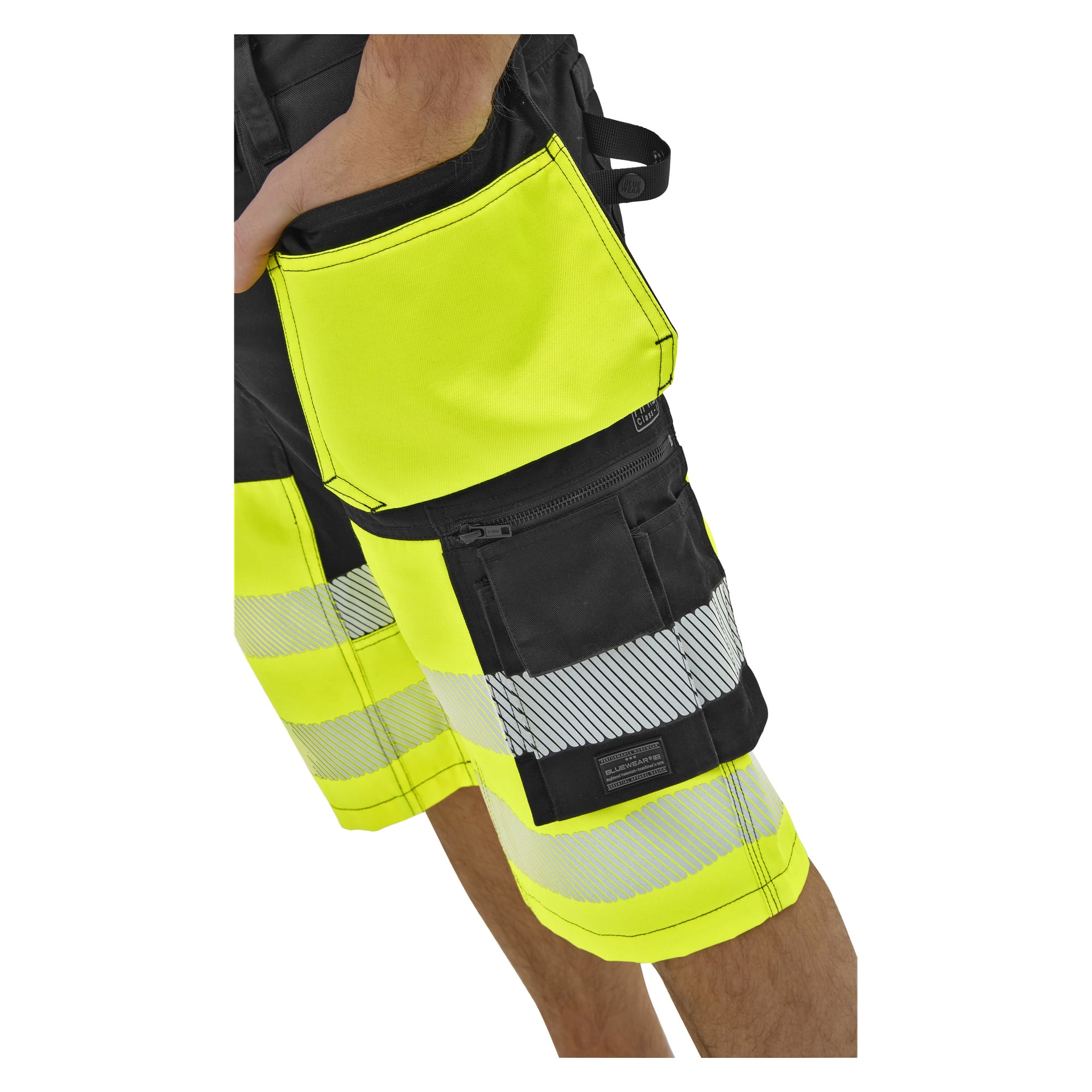 En person klädd i svart och neongula hög-vis-shorts med silverfärgade reflekterande ränder, en stor framficka och en zip-ficka.