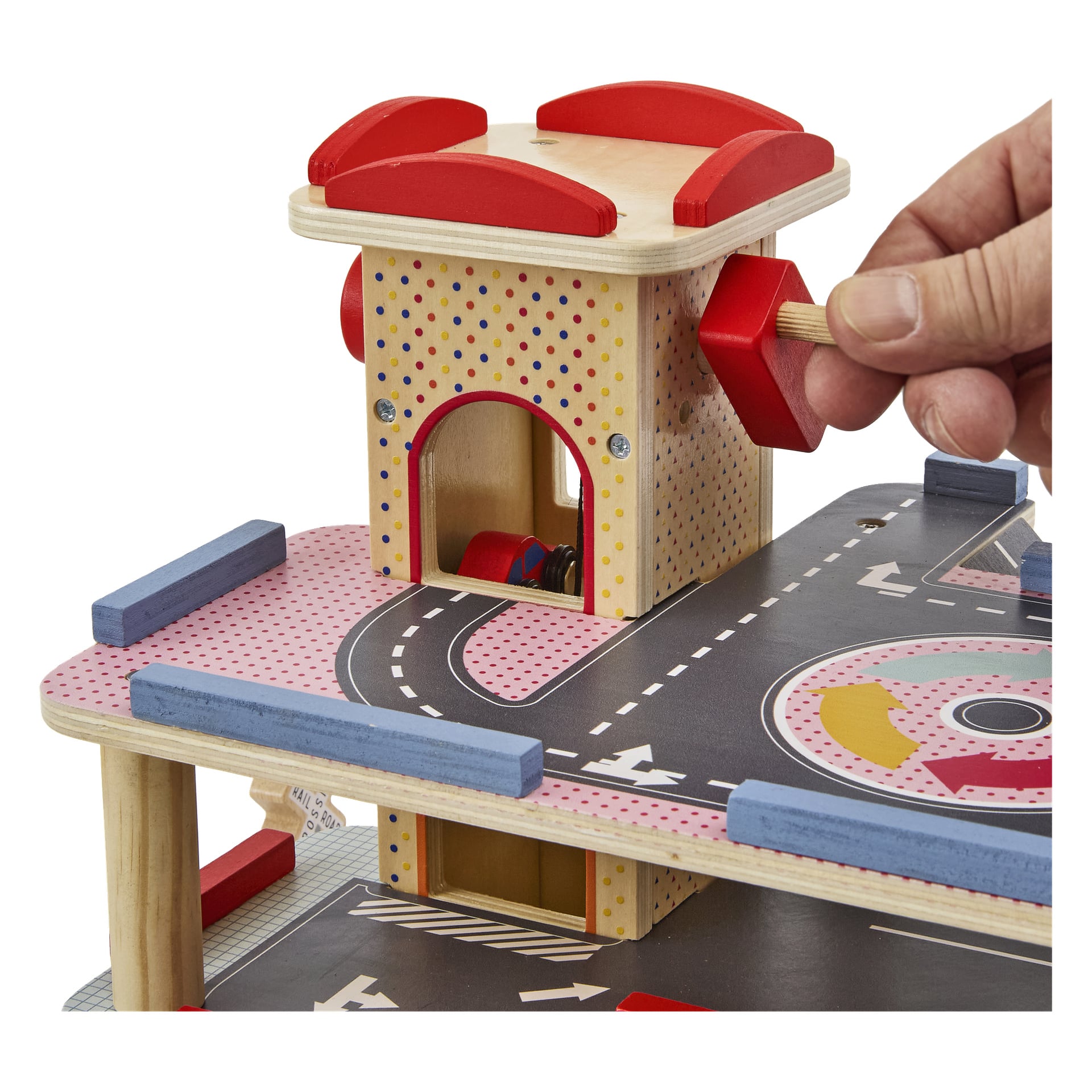 Eine Hand dreht einen roten Griff auf einer bunten hölzernen Spielzeugparkgarage mit Rampen, gestrichenen Straßen und einem kleinen Auto im Aufzug.
