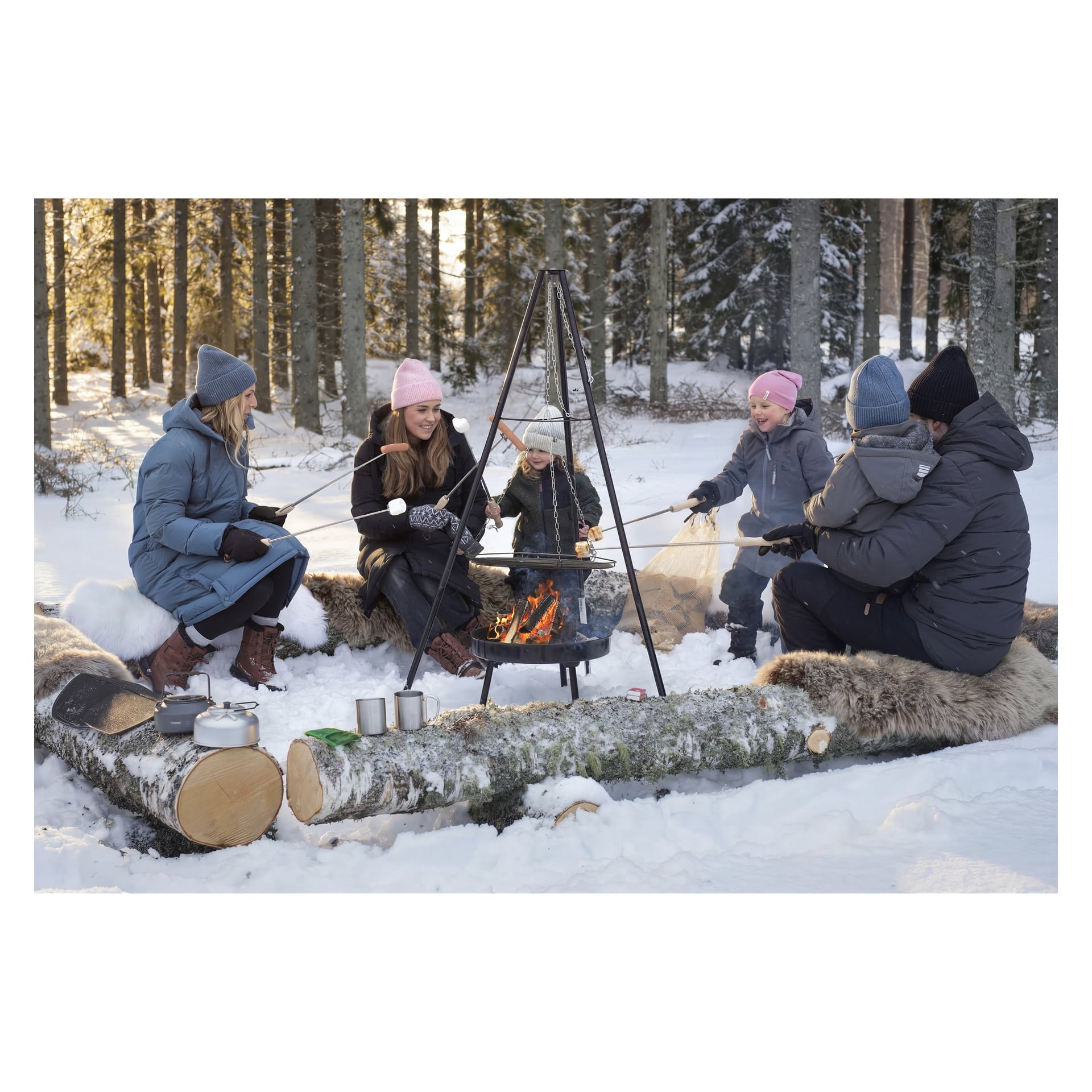 Fem personer i vinterkläder sitter på stockbänkar vid en snötäckt lägereld och rostar mat. Krukor och koppar vilar på stockarna i närheten.