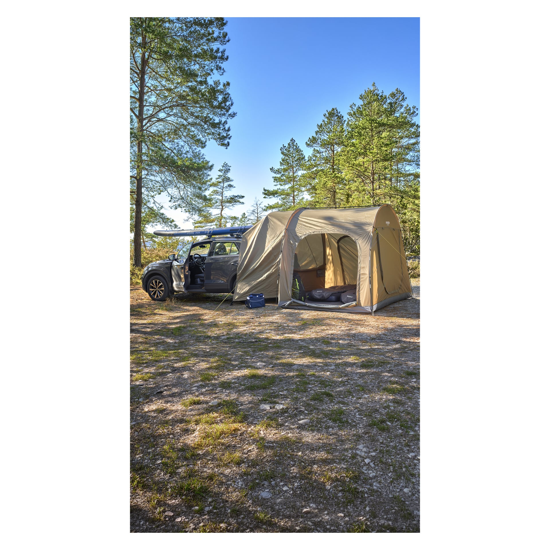 En bil med ett tält står på en jordglänta bland höga tallar under en blå himmel, med campingutrustning i närheten.