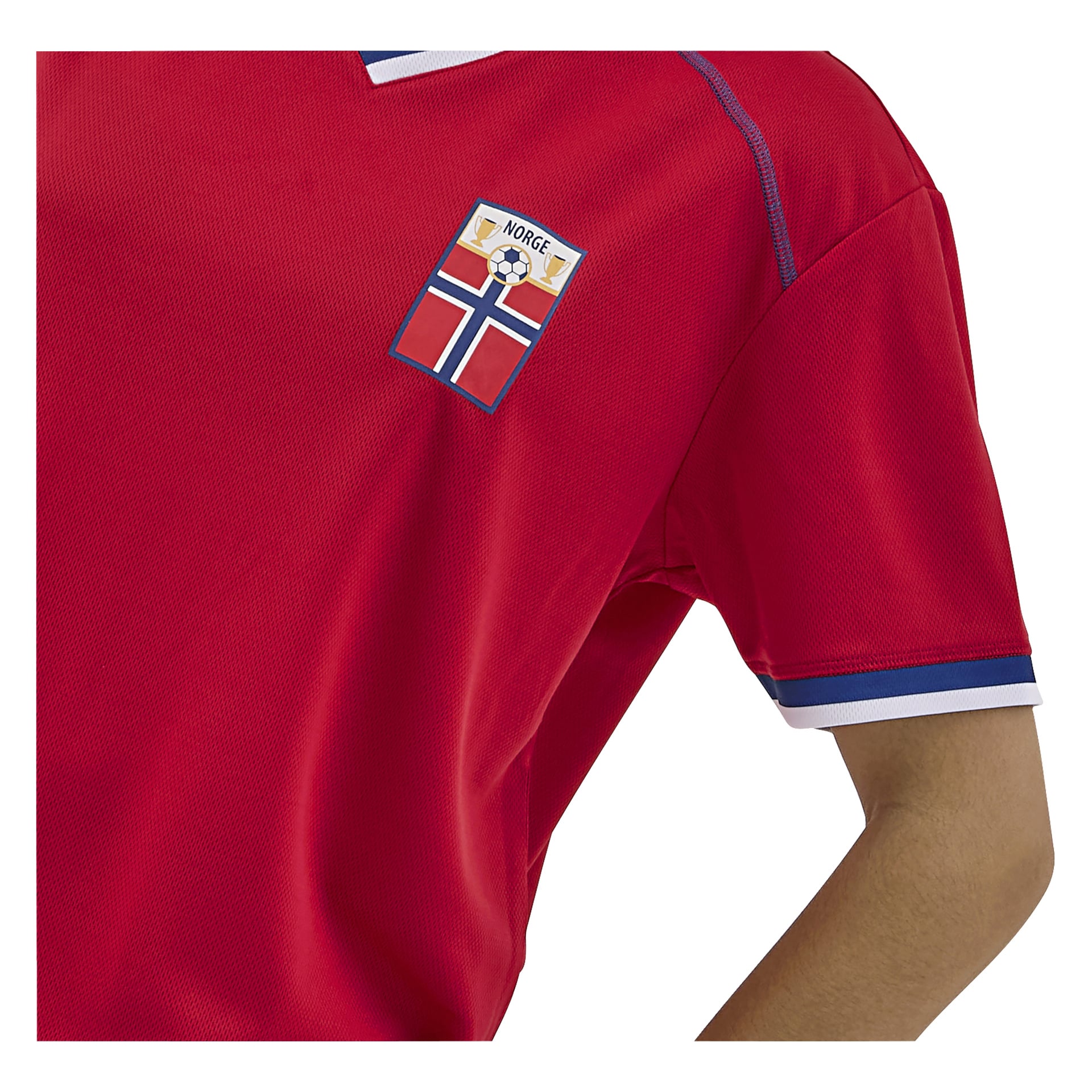 En person i en rød sportsdrakt med blå og hvit kant. Et merke på brystet viser en fotball, "Norge," og flagget.