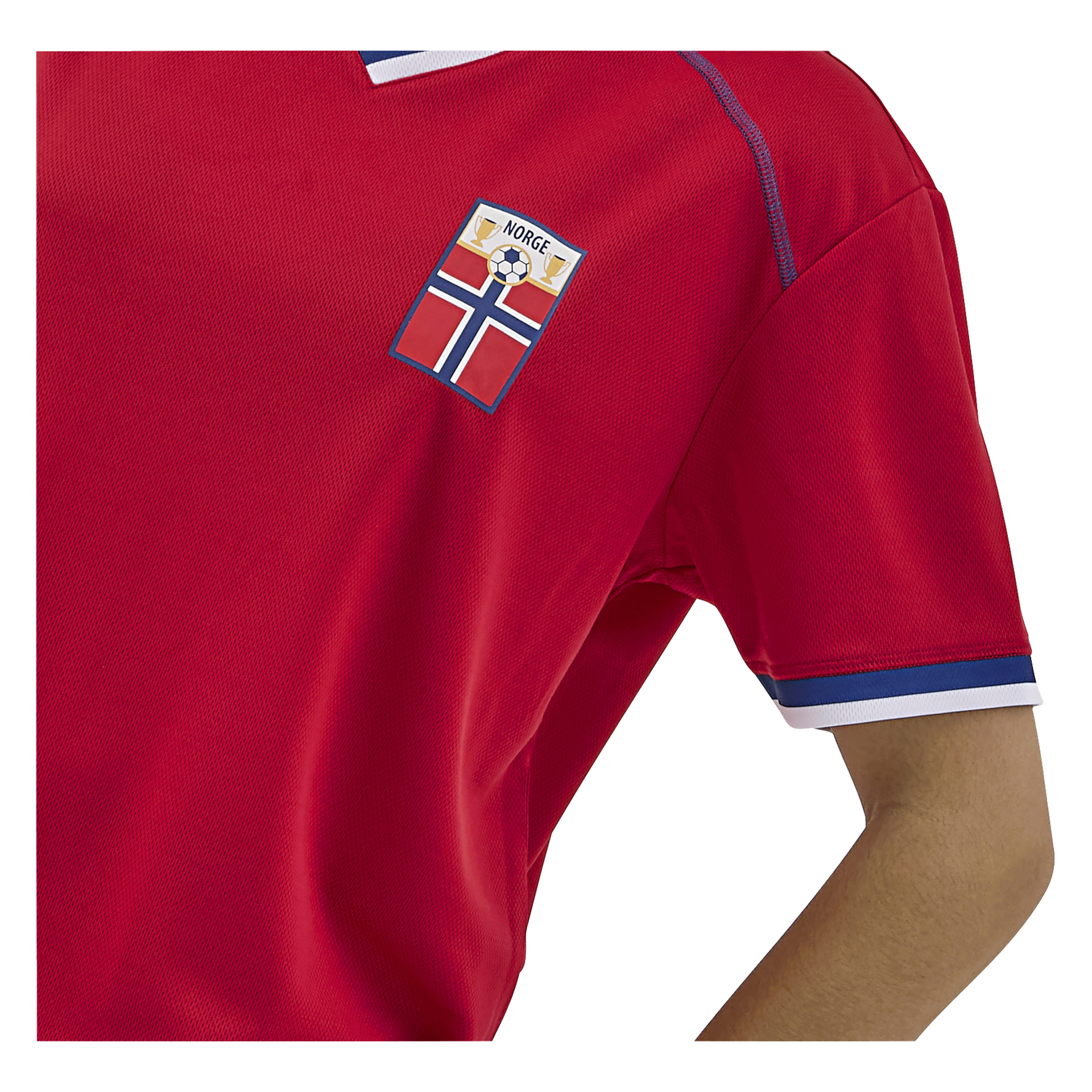En person i en rød sportsdrakt med blå og hvit kant, med en fotballlapp og det norske flagget merket "Norge" på brystet.