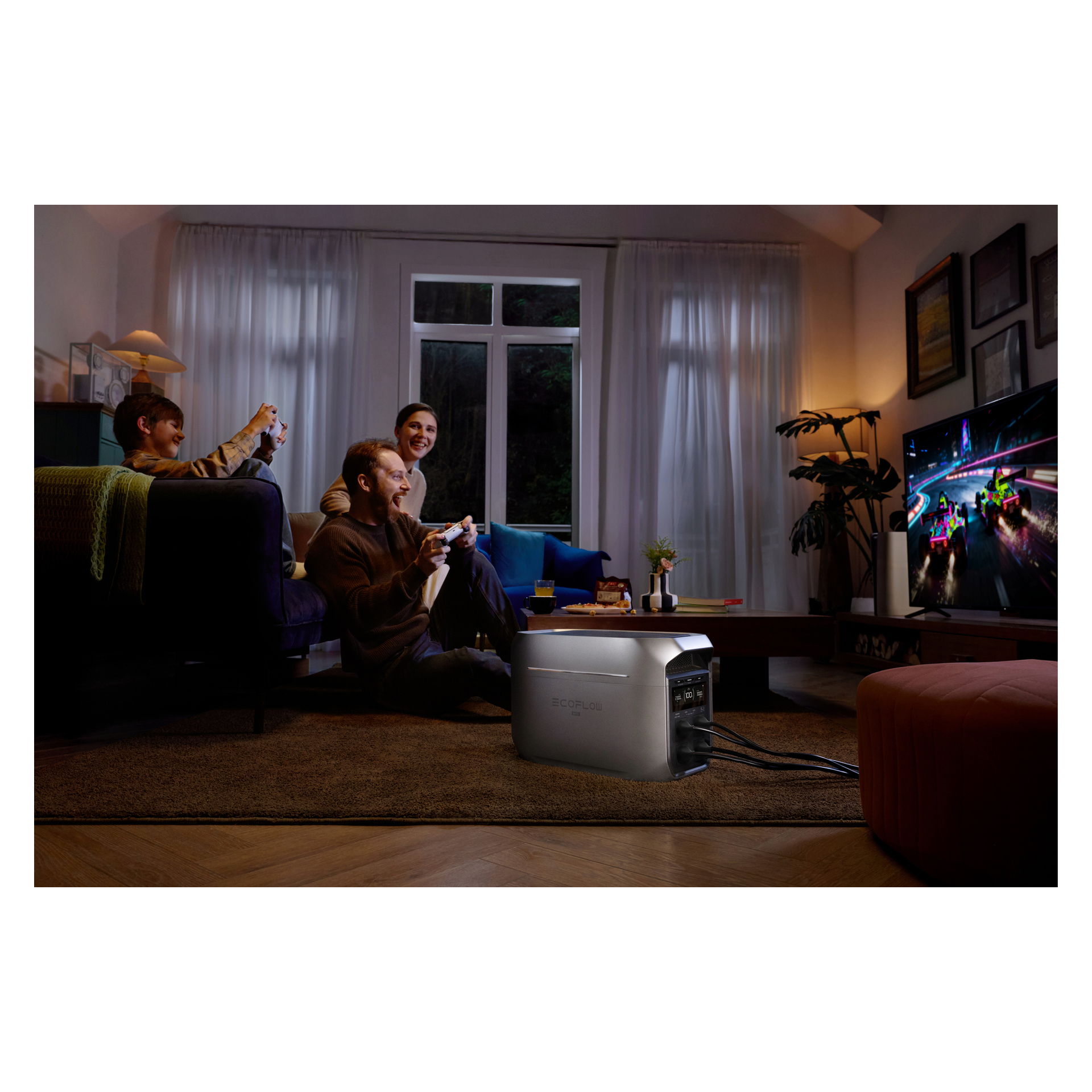 Kolme ystävää pelaa videopelejä öisin kodikkaassa, hämärästi valaistussa olohuoneessa. Lattialla oleva hopeinen voimalaitos antaa sähköä televisiolle.