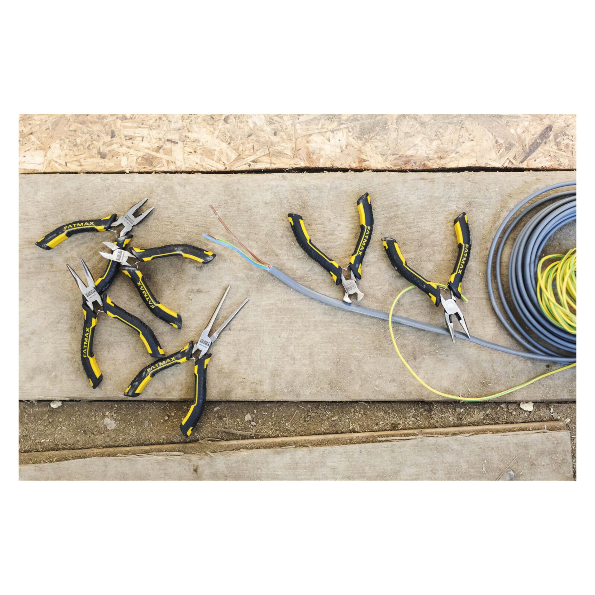 Sju tänger på träbrädor, två som greppar en grå kabel. En spole av elektrisk ledning sitter till höger på en byggarbetsplatsyta.