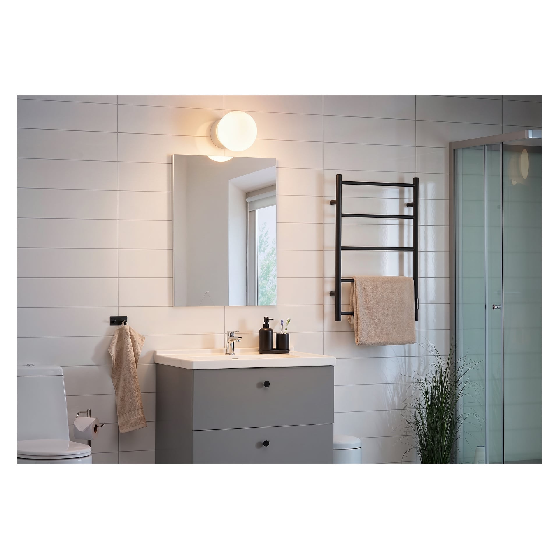 Modern badrum med vita kakel, grått kommod, rektangulär spegel, vägglampe, glasdusch, handdukshängare, toalett och krukväxt.
