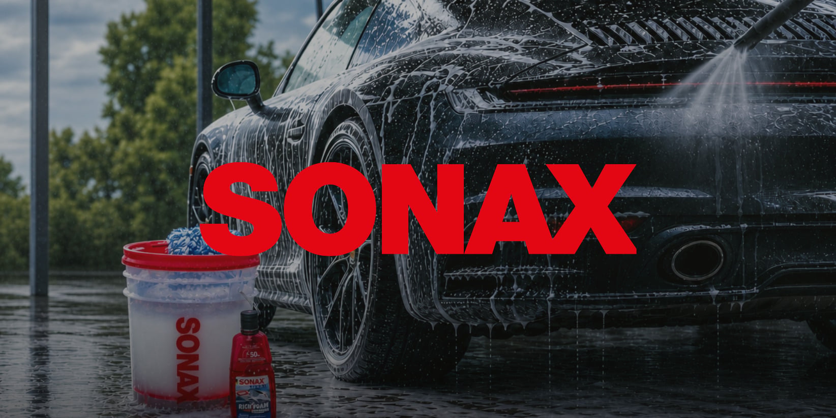 En svart sportbil som tvättas med tvål; SONAX rengöringsprodukter och en röd SONAX-logga är tydligt synliga i förgrunden.