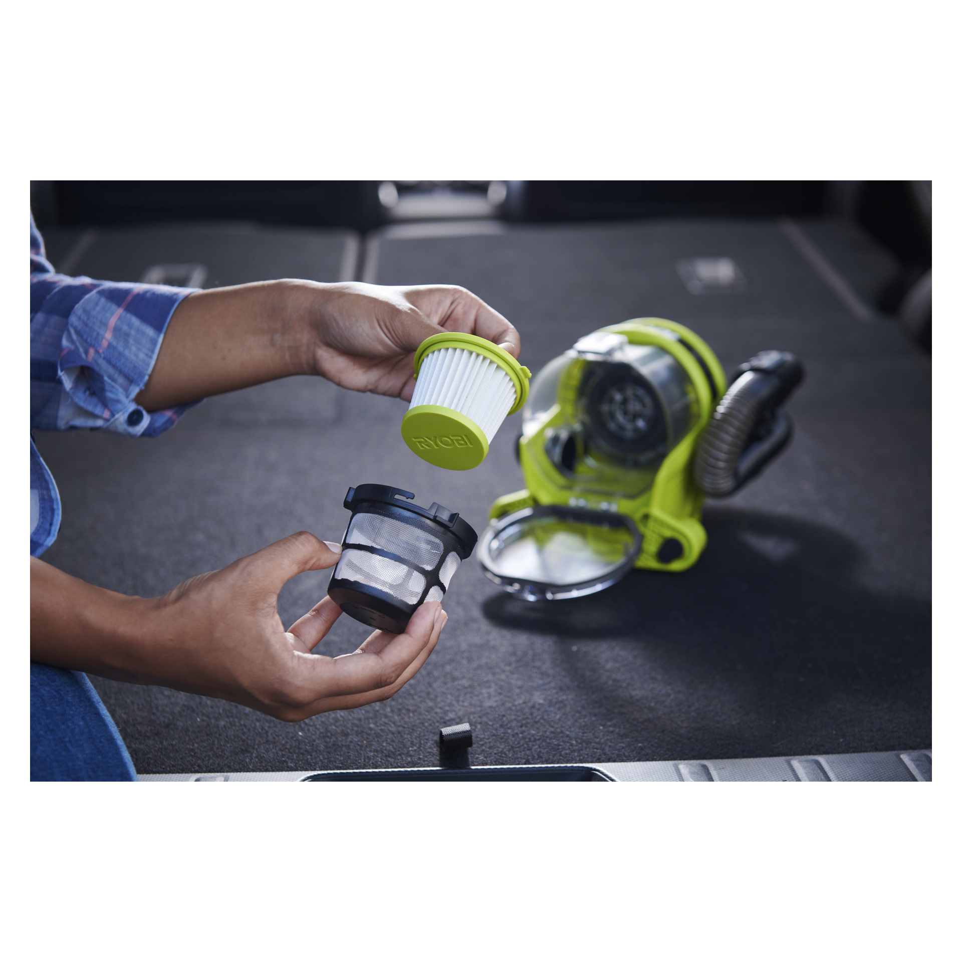 Et par hender holder et vakuumfilter og en nettnettskjerm, mens en Ryobi One+ batteridrevet bilstøvsuger RAV 1805-0 hviler på et mørkt teppe i bakgrunnen.