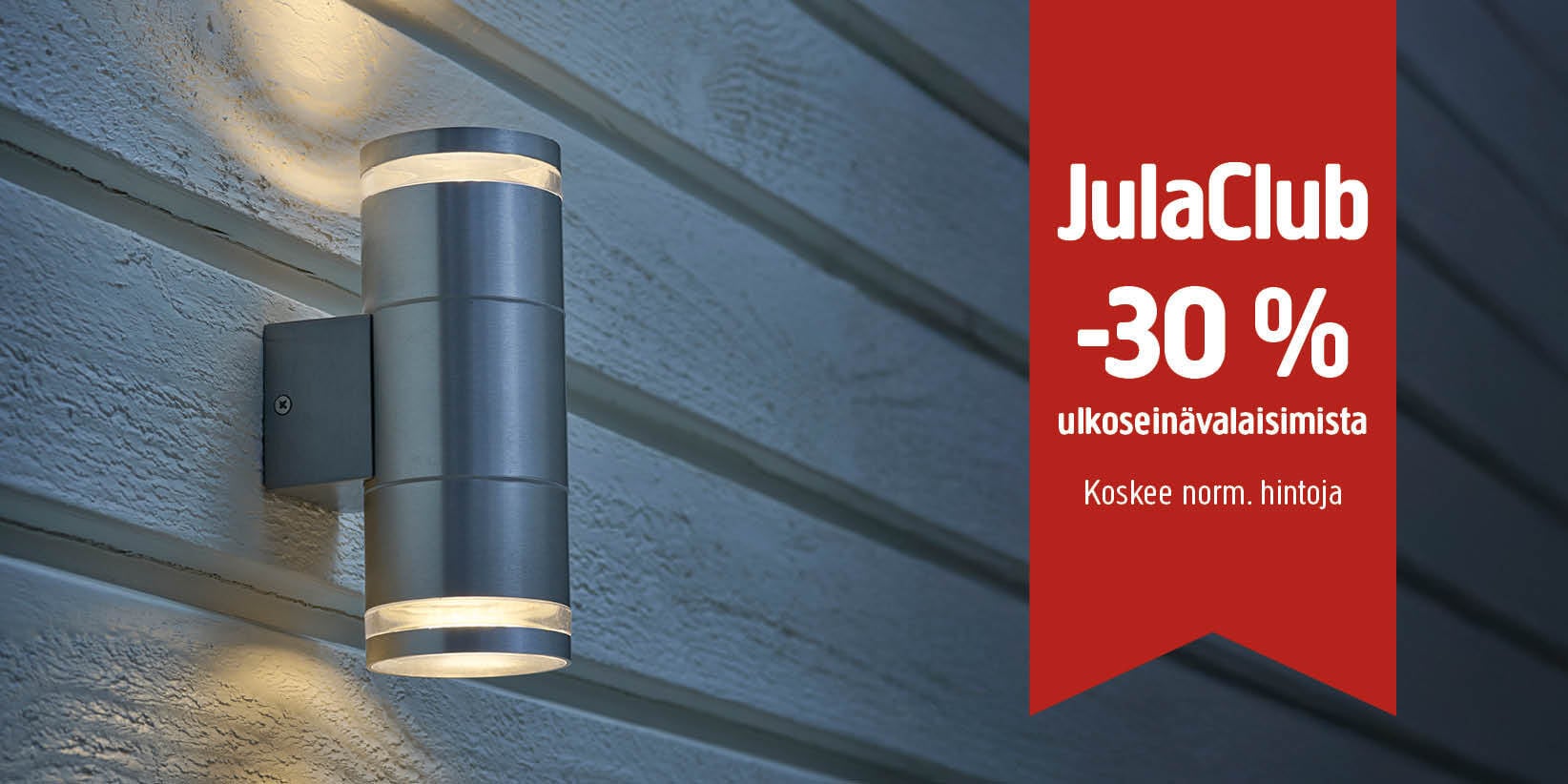 Puupaneeliseinään kiinnitetty sylinterimäinen ulkoseinävalaisin sijaitsee punaisen banderollin vieressä, jossa lukee: ”JulaClub –30 % ulkoseinävalaisimista. Koskee normaalihintoja.”.