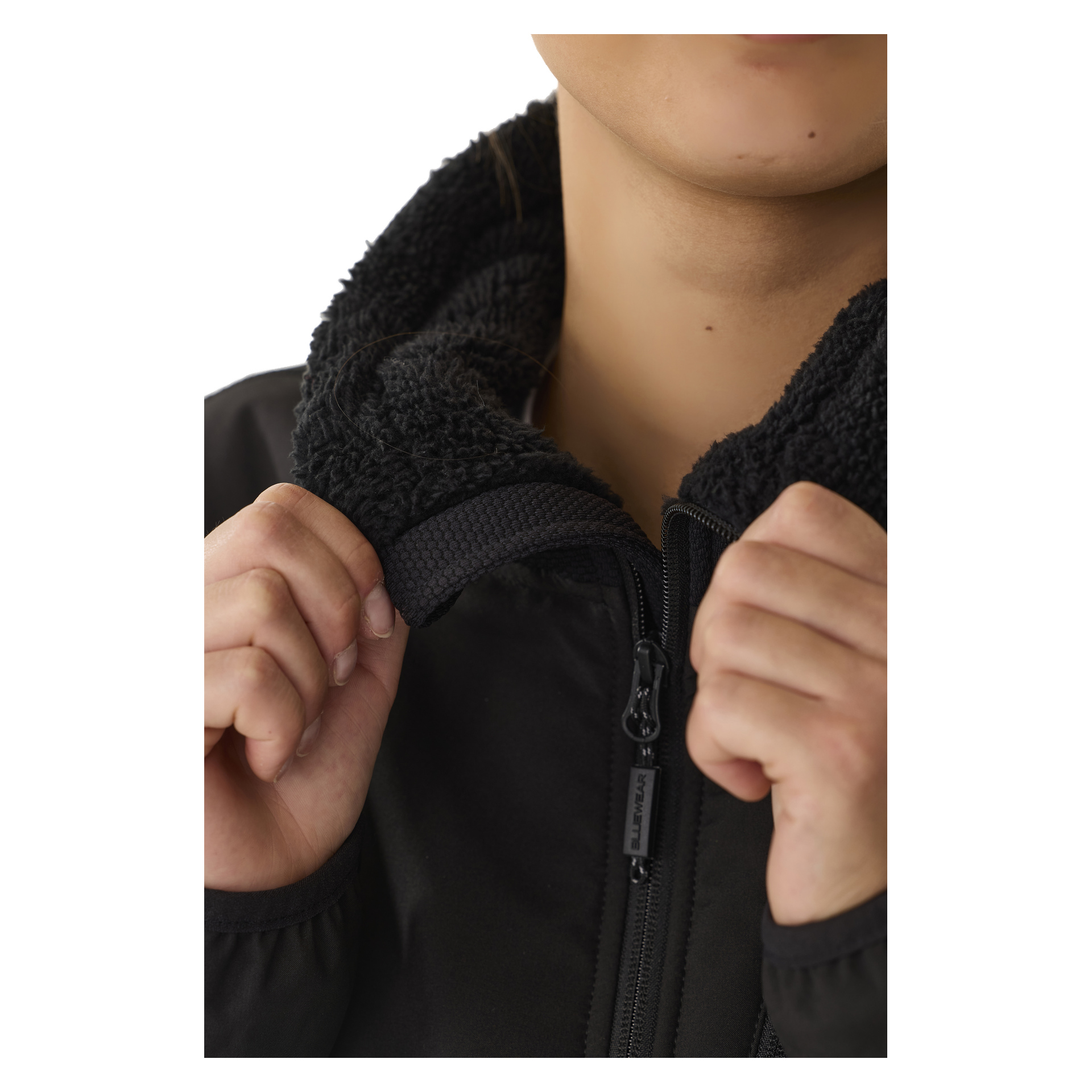 En person griper tak i kragen på en delvis glidelåst svart Bluewear Women's Moa fleecejakke med luvfôr, slik at bare den nedre halvdelen av ansiktet og hendene vises.