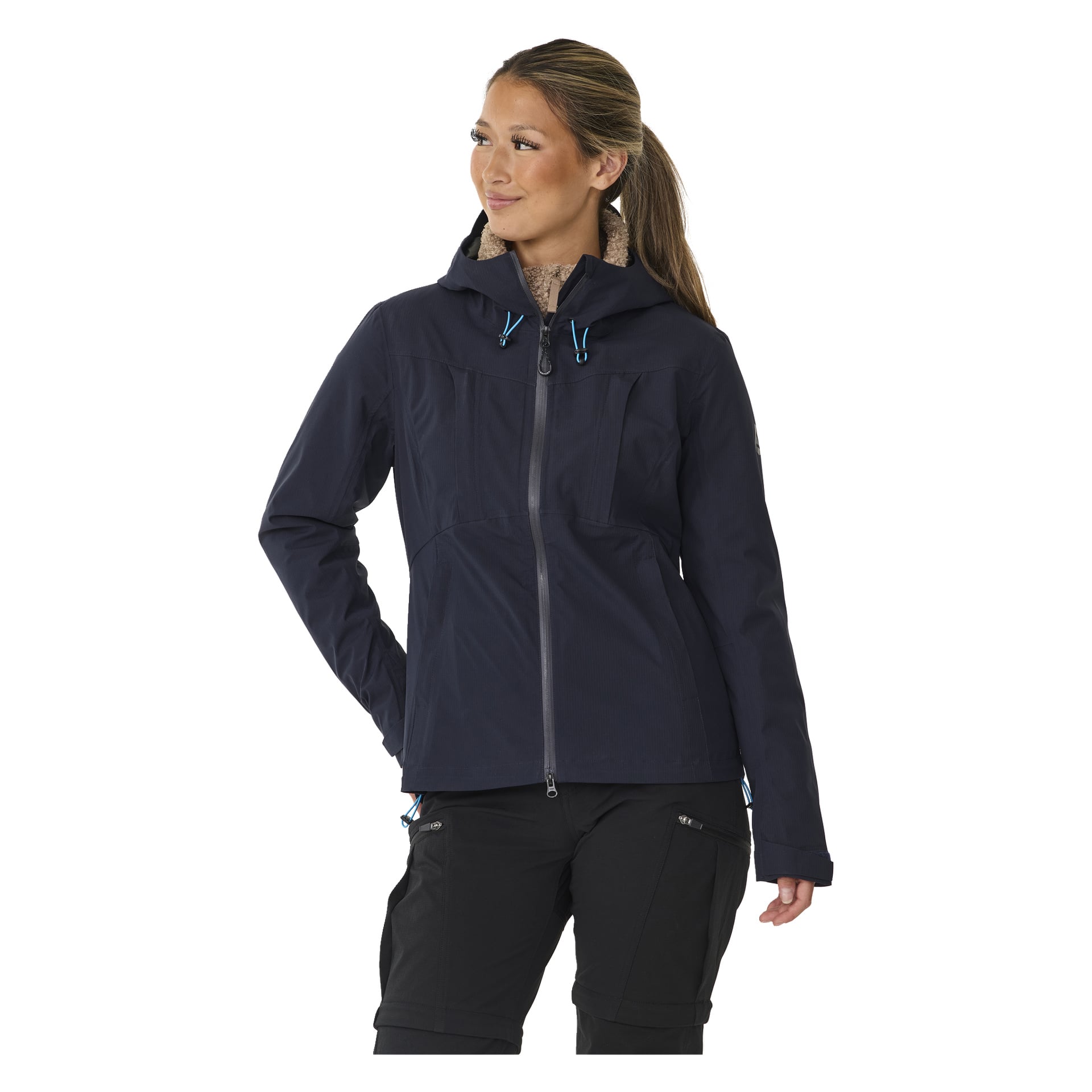 Eine Frau steht mit einer Hand in der Tasche und schaut zur Seite. Sie trägt die Kayoba Outdoor Women's Shell-Jacke Sarek, die dunkel mit blauen Kordeln ist, und schwarze Hosen.