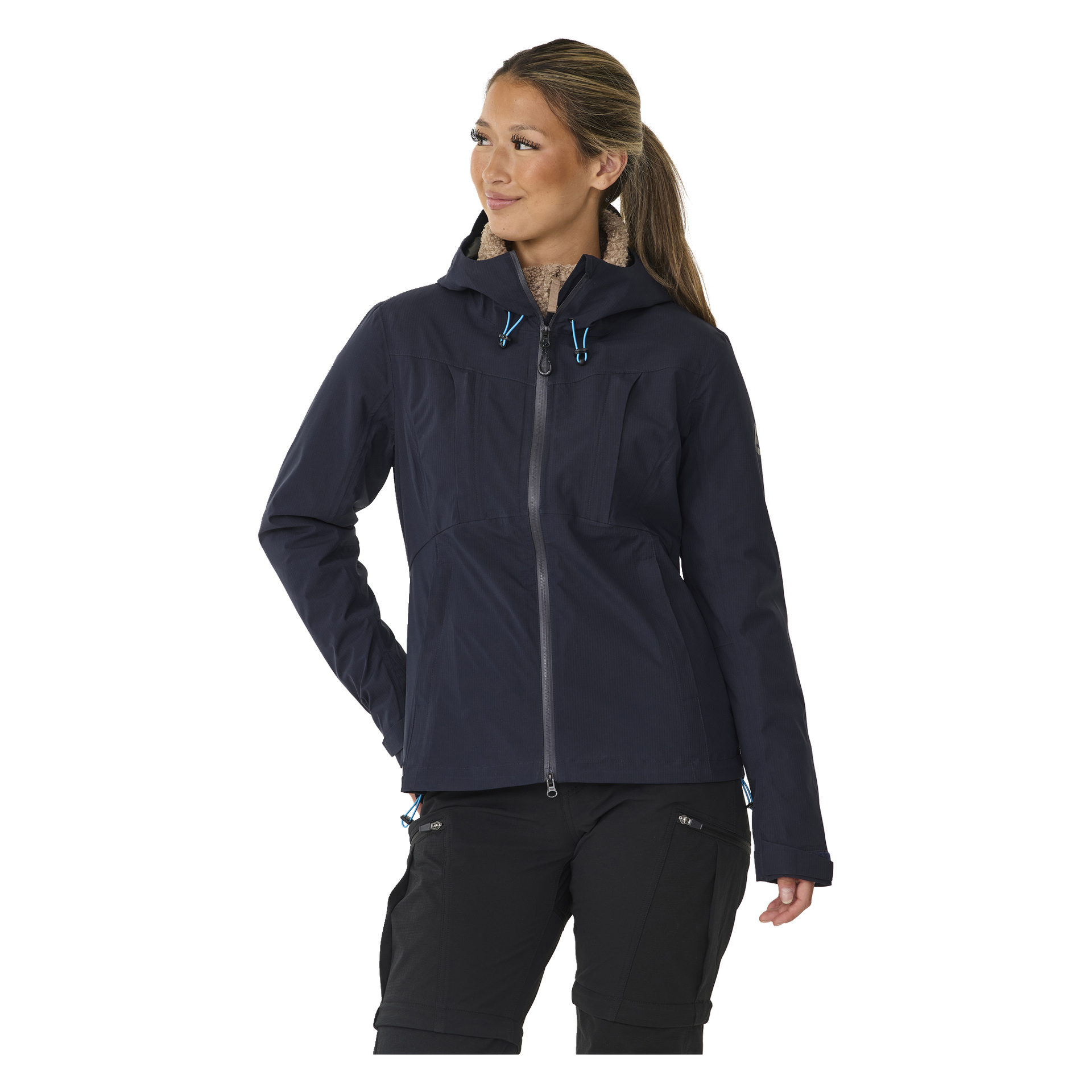Eine Frau präsentiert die Kayoba Outdoor Women's Shell Jacket Sarek, die eine dunkle Kapuze und blaue Kordeln hat, kombiniert mit schwarzen Hosen. Sie hat eine Hand in der Tasche und blickt zur Seite.