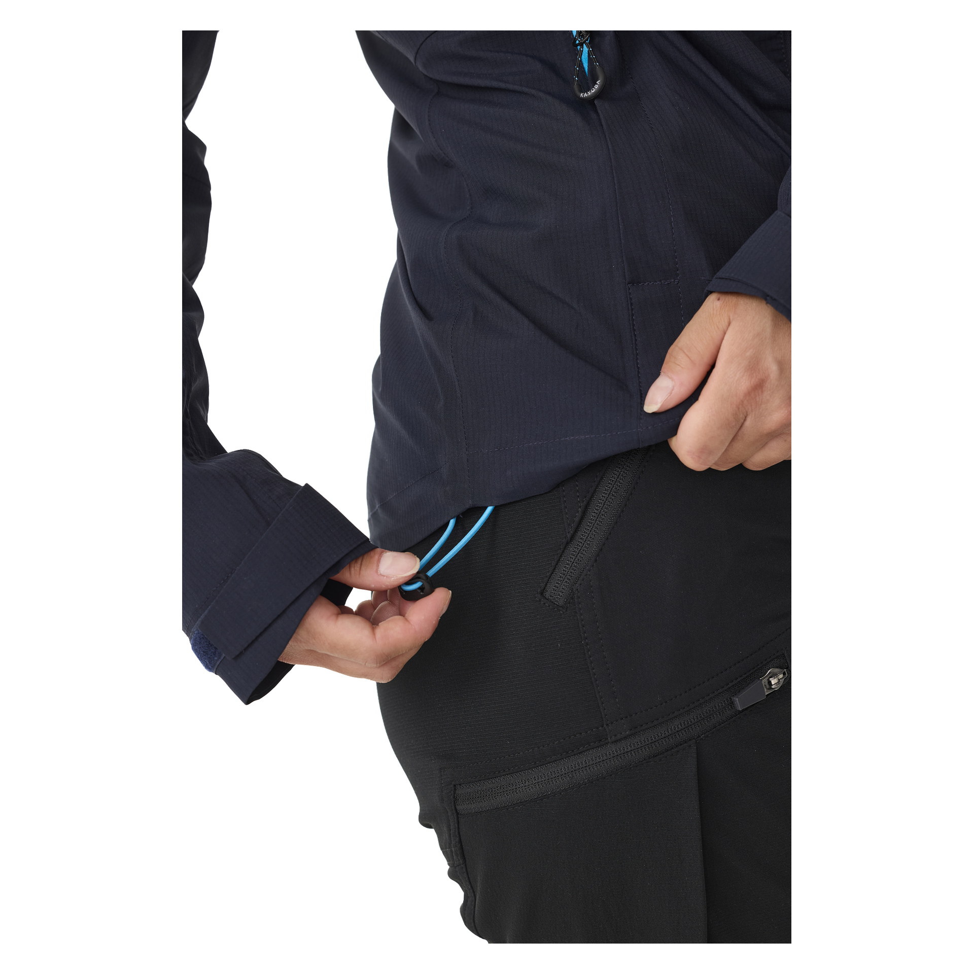 Eine Person zieht an der blauen Saum-Kordel, um die Passform einer Kayoba Outdoor Damen-Shelljacke Sarek an der Taille anzupassen, während die andere Hand auf einer Reißverschlusstasche schwarzer Hose ruht. Das Bild zeigt nur ihren Oberkörper und ihre Hände.