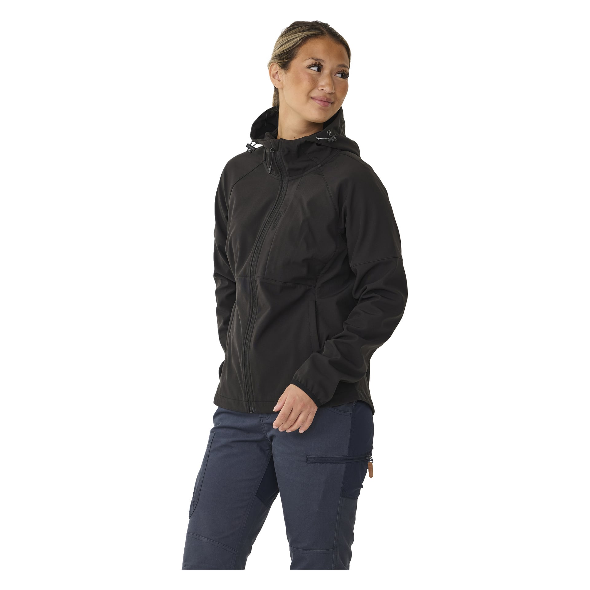Eine Person, gekleidet in die mit Fleece gefütterte Softshelljacke Hede von Kayoba Outdoor Women's und dunkelblaue Cargohosen, steht leicht schräg und blickt nach links, mit einem Arm an der Seite und der anderen Hand an einer Tasche.
